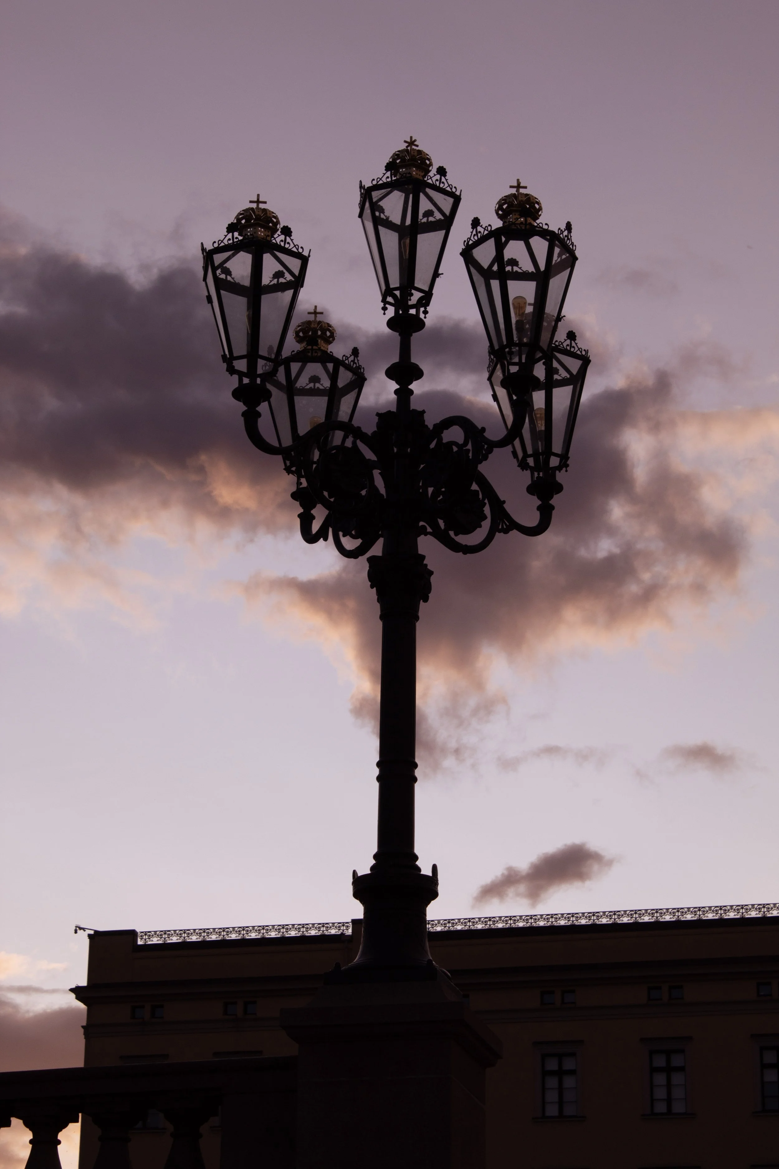 Silhouette of an ornate street lamp with multiple lanterns against a purple and pink sunset sky with clouds.
