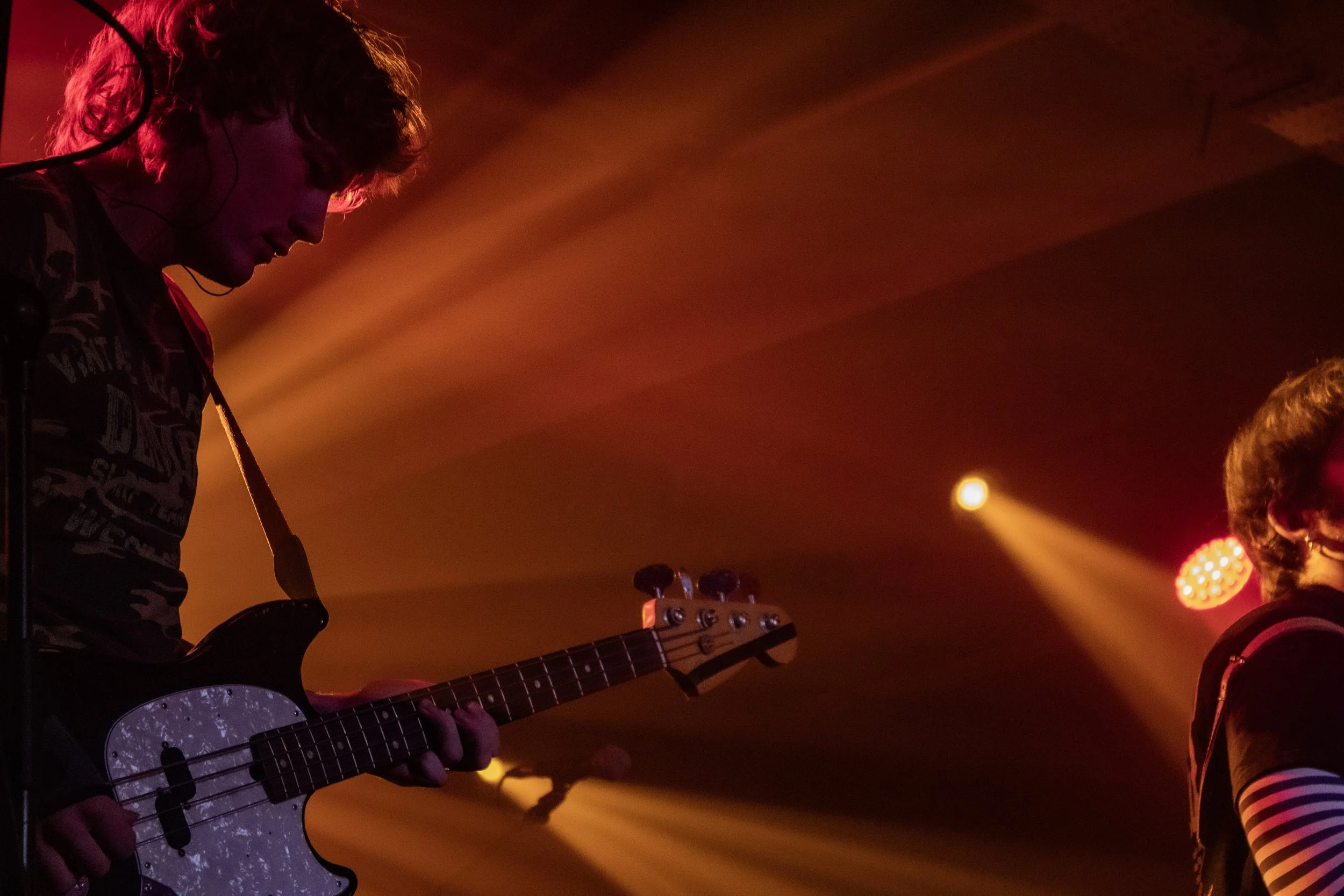 A musician playing an electric guitar on stage with orange and yellow stage lighting.