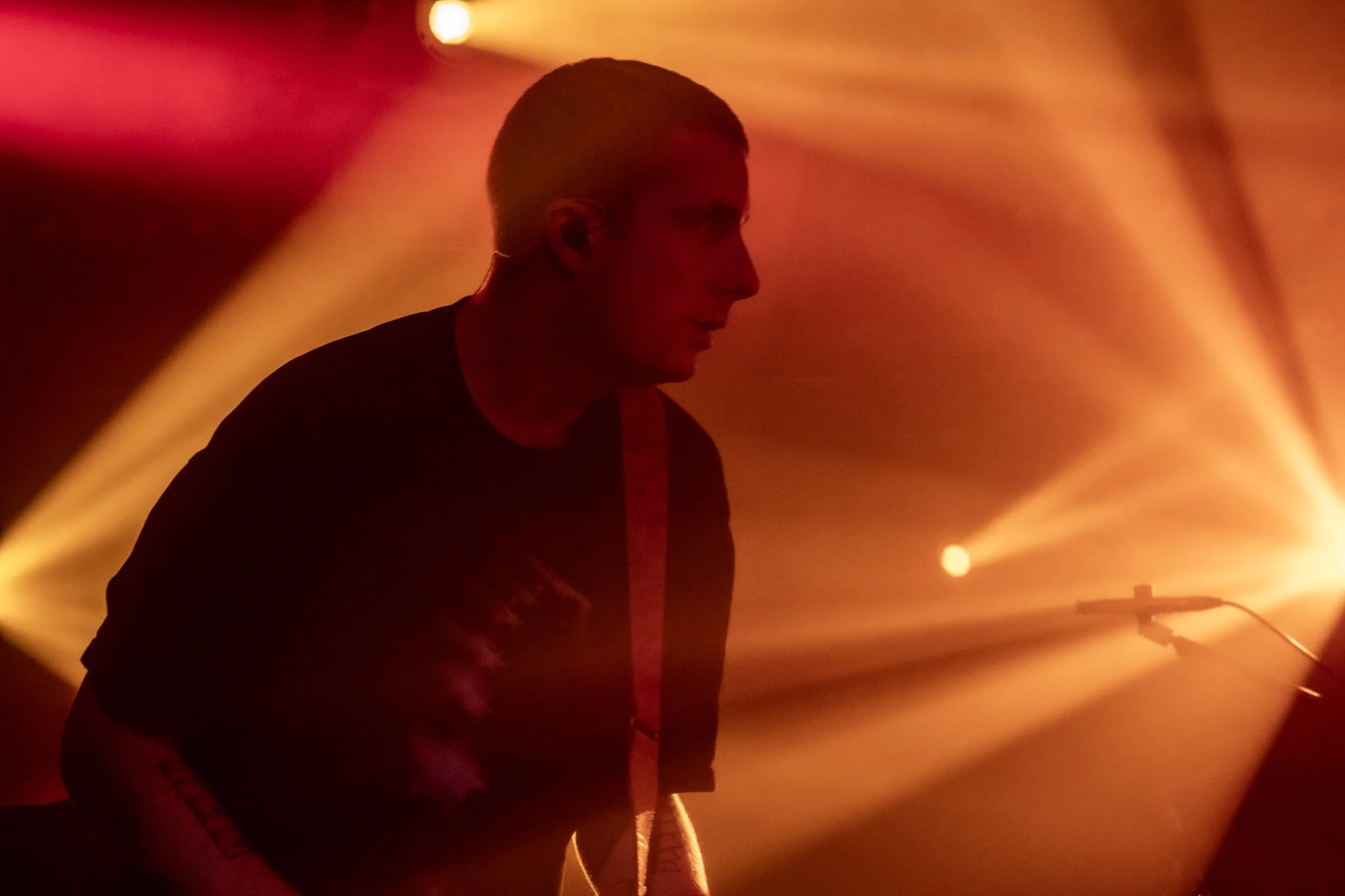 A person playing guitar on stage, illuminated by vibrant orange and yellow stage lights.