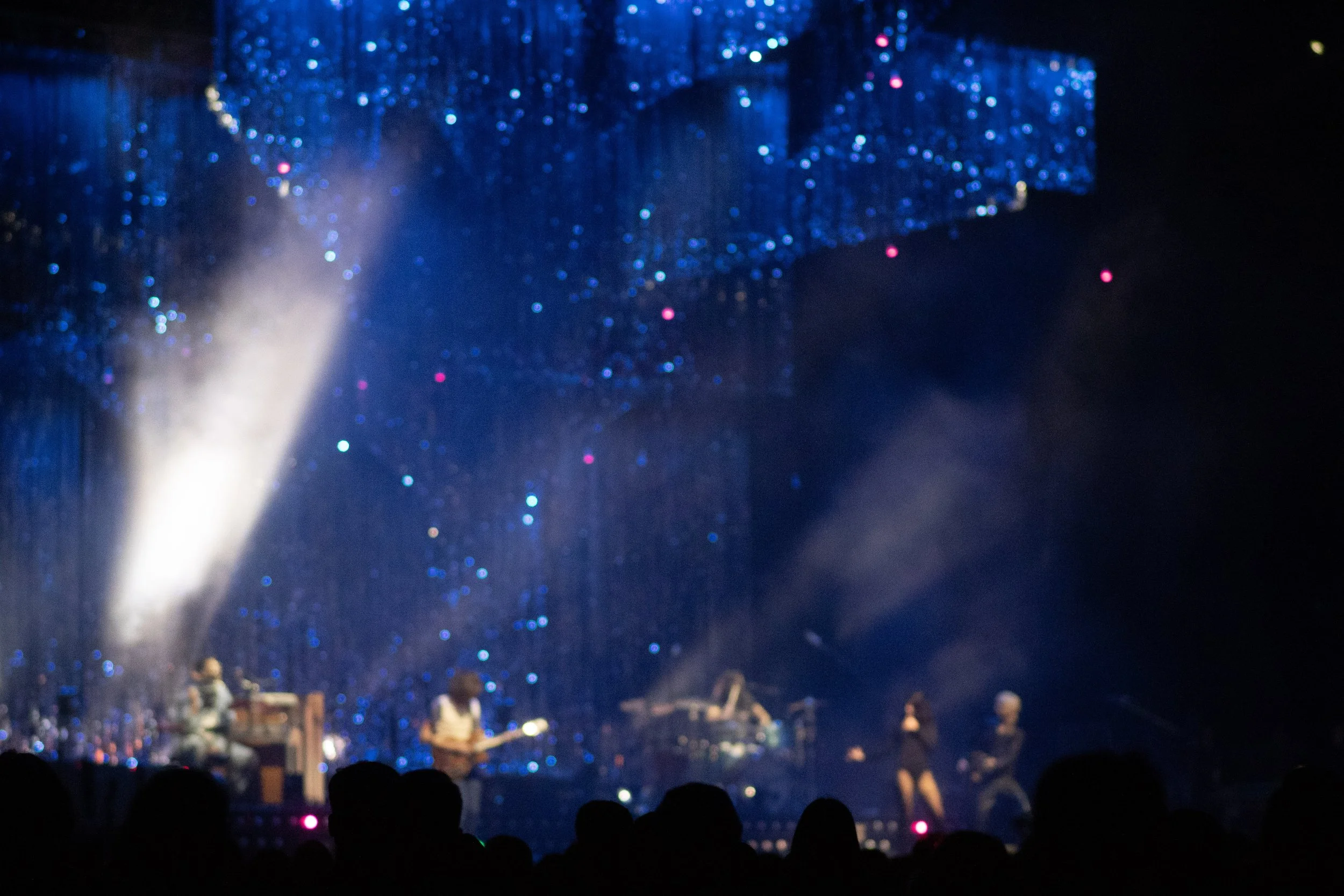 Stage with performers, blue and purple lighting, and audience silhouettes