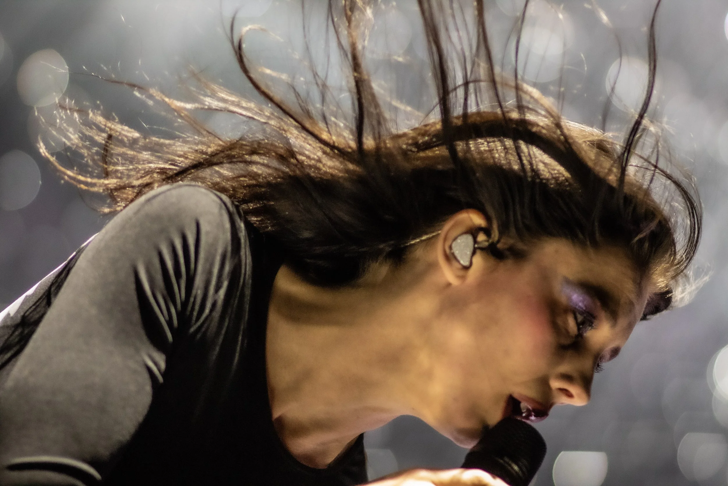 A female singer with wet hair holding a microphone and singing on stage, with blurred background lights.