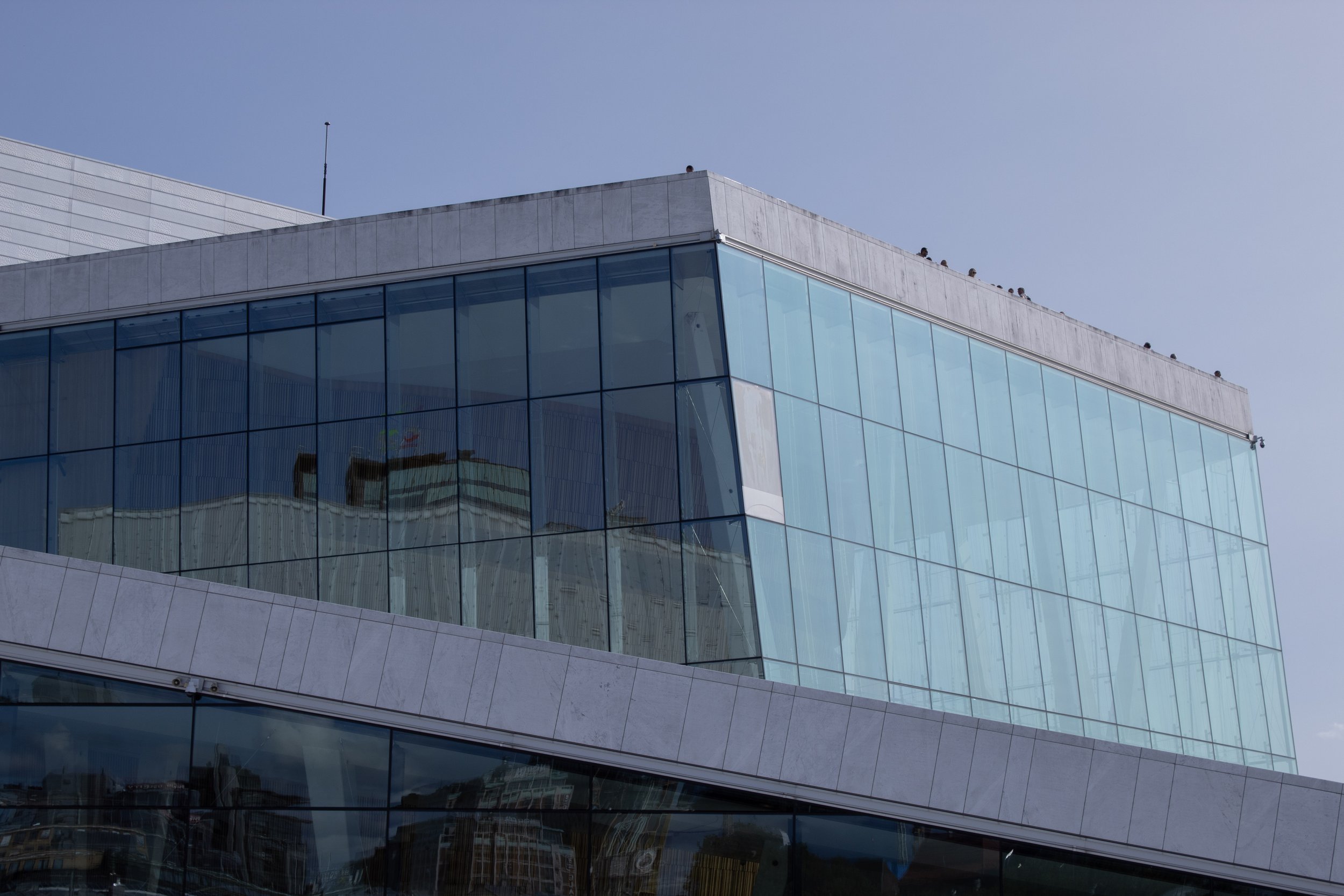 Modern building with large glass windows reflecting surrounding structures, with a clear blue sky above.