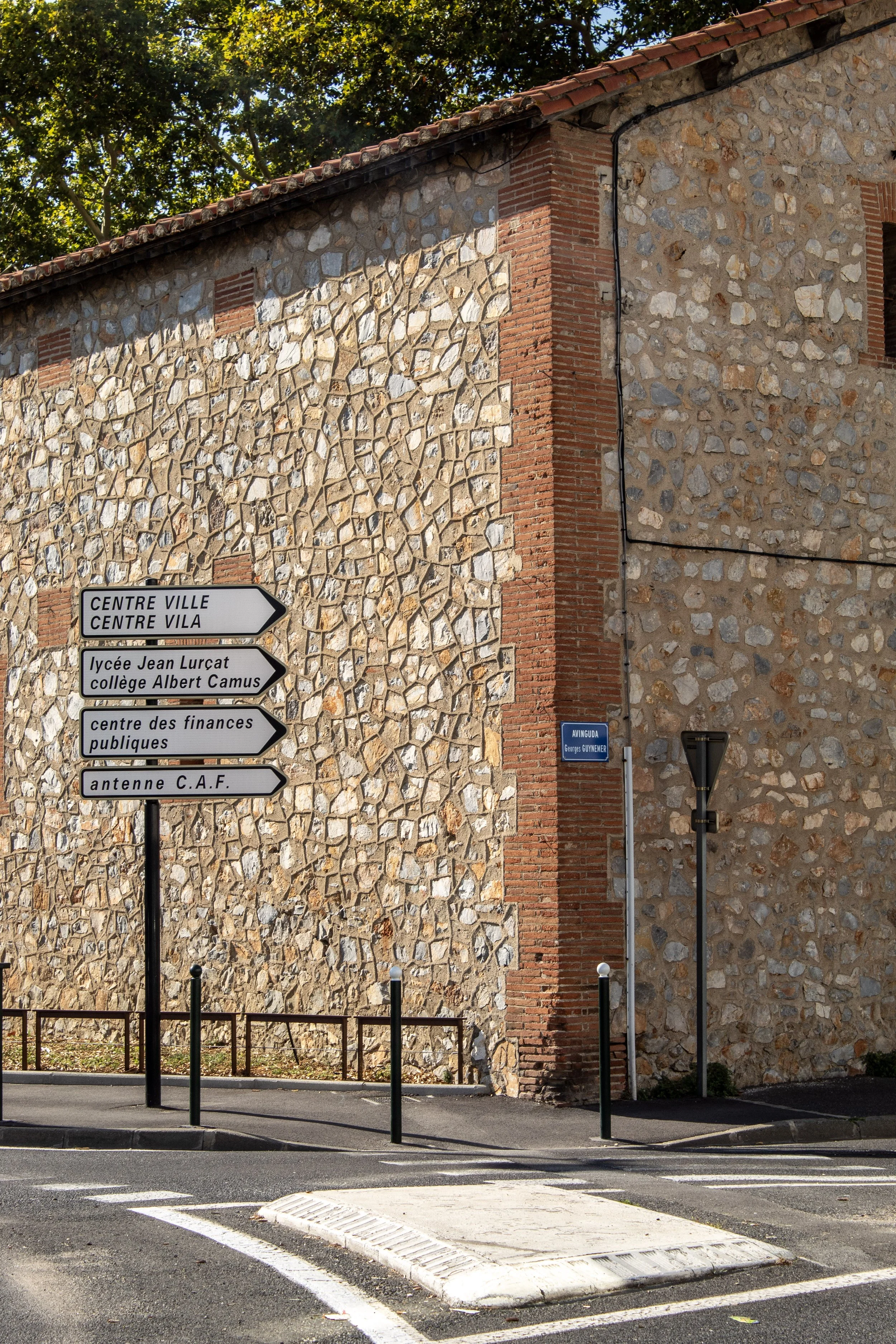 Street corner with directional signs pointing to the city center, high school, and public finance center, against a background of old stone and brick building with a blue street sign and streetlight