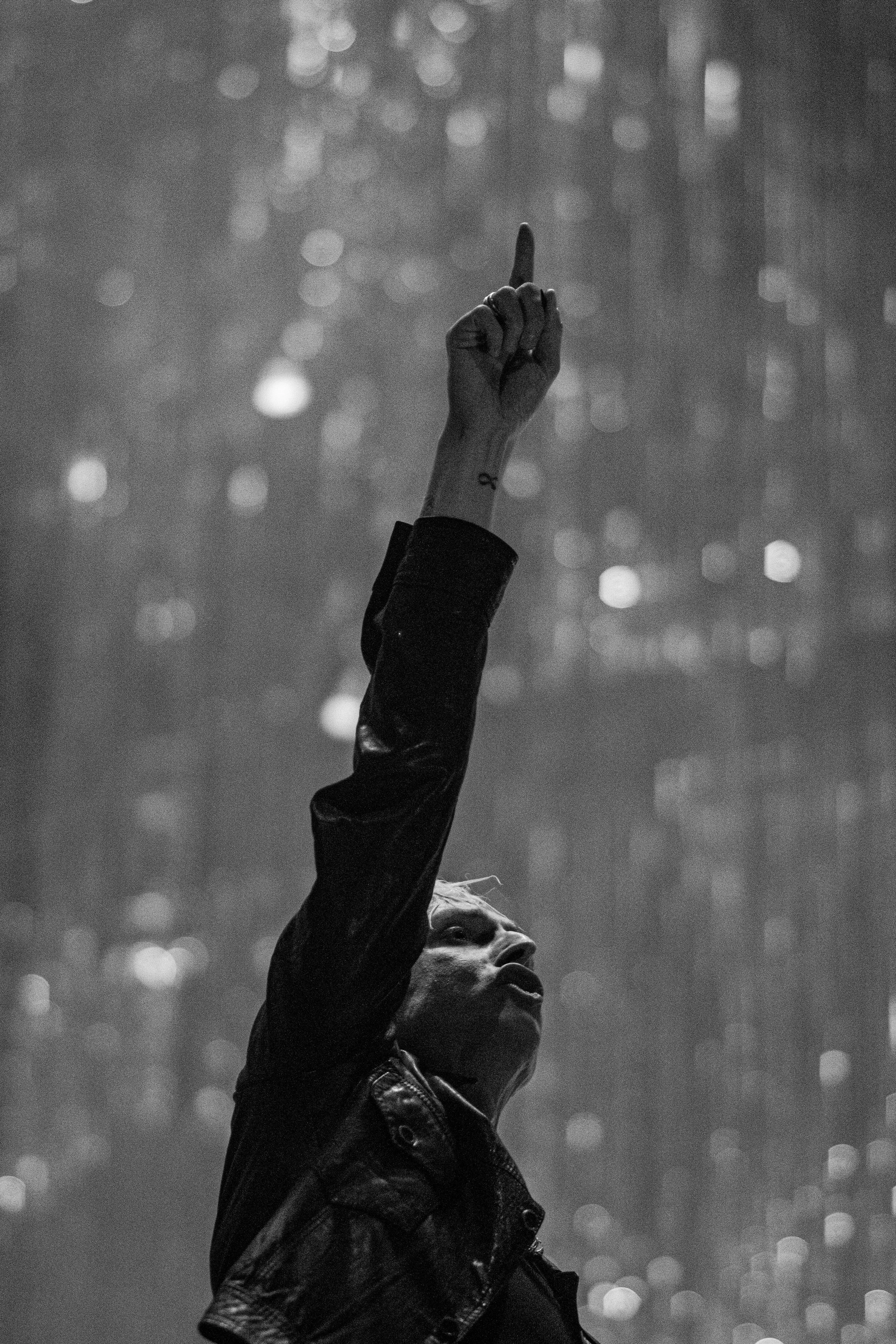 A person in a leather jacket raising their middle finger against a blurred cityscape background