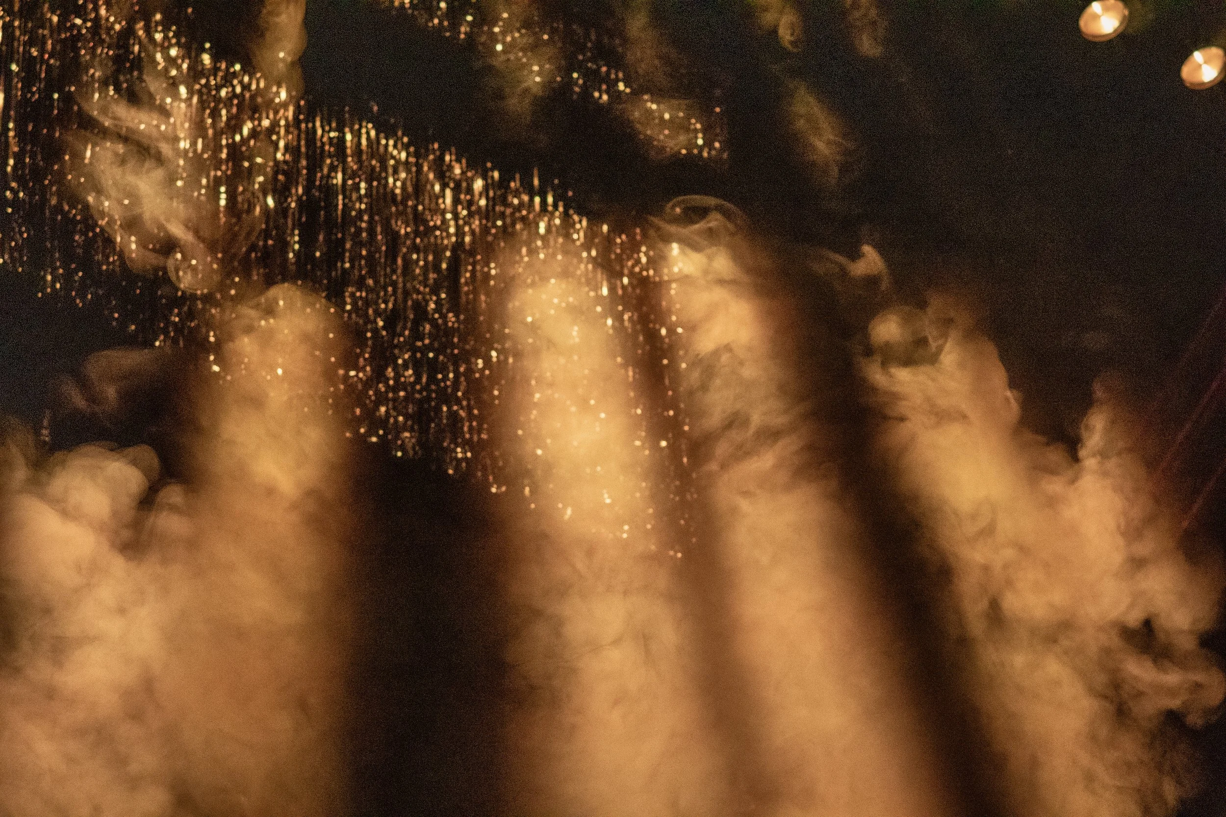 Close-up of a waterfall illuminated with golden light, creating a shimmering effect with cascading water and mist in darkness.