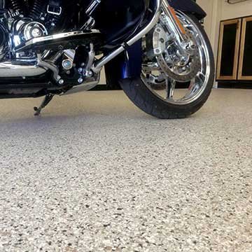 Close-up of the front wheel and part of the body of a motorcycle on a garage floor.