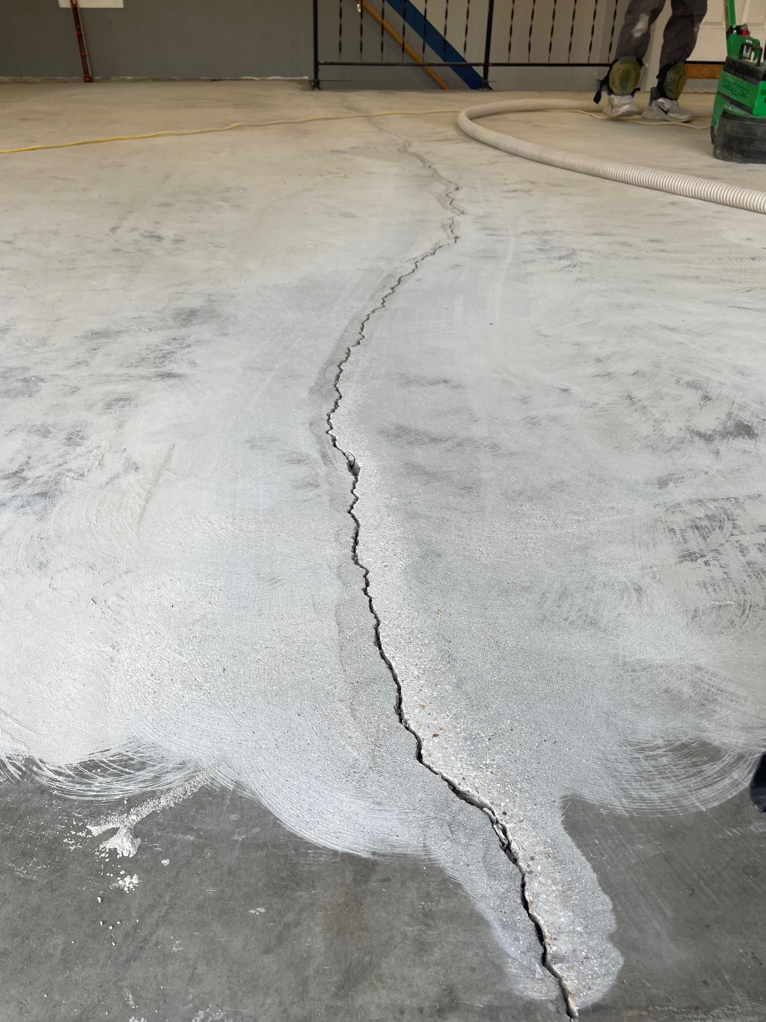A large crack runs through a concrete floor at a construction site. Construction tools and equipment are visible, and a worker is standing in the background.