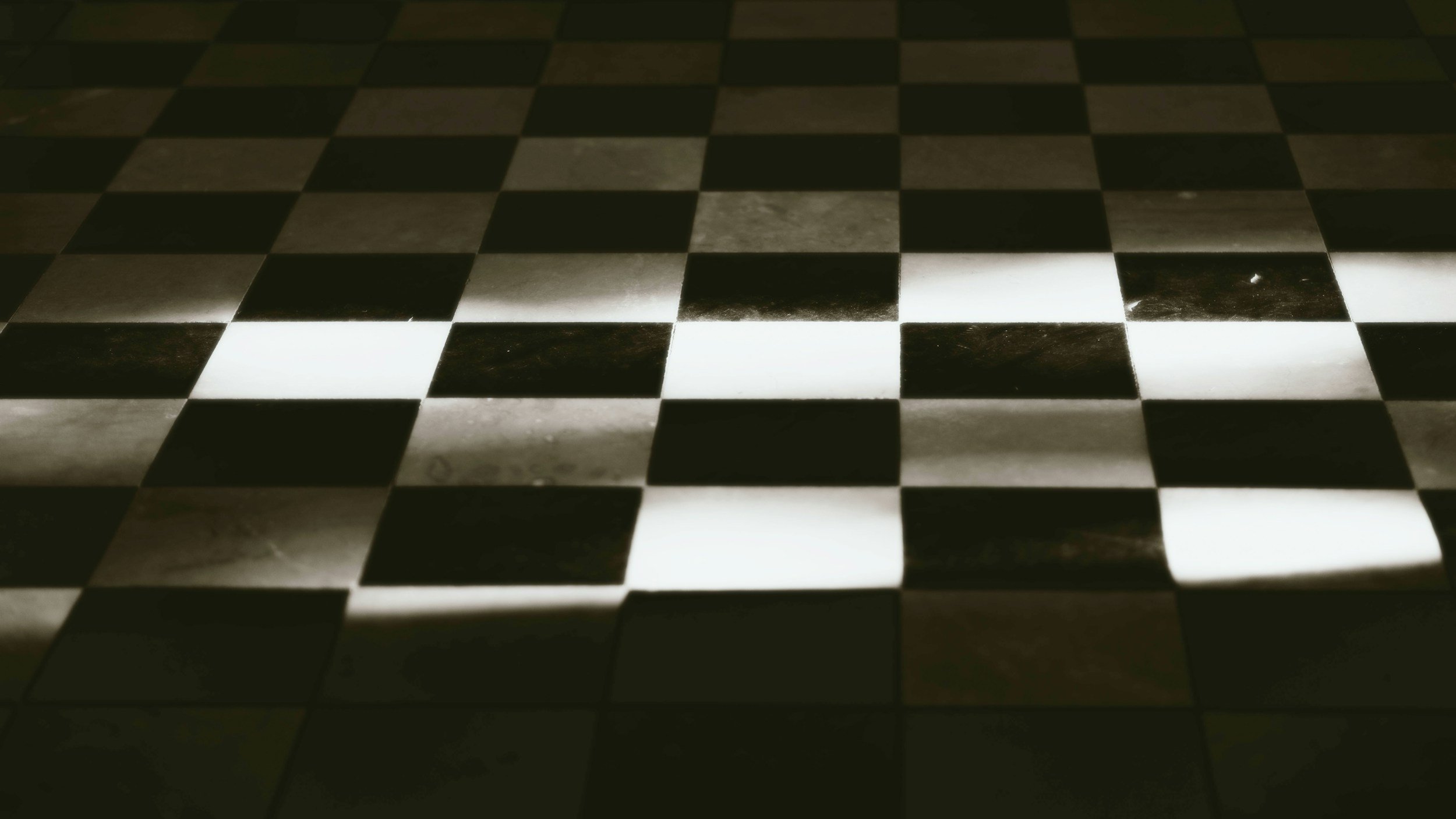 A black and white checkered chessboard with light shining on some squares.