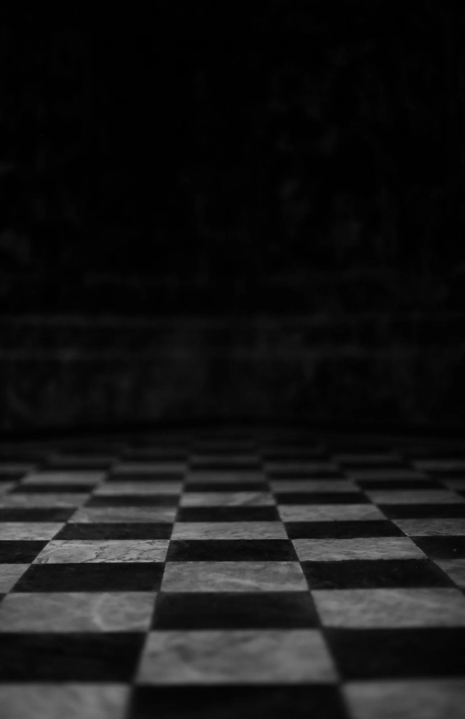 Close-up view of a black and white checkered tiled floor with the background obscured in darkness.