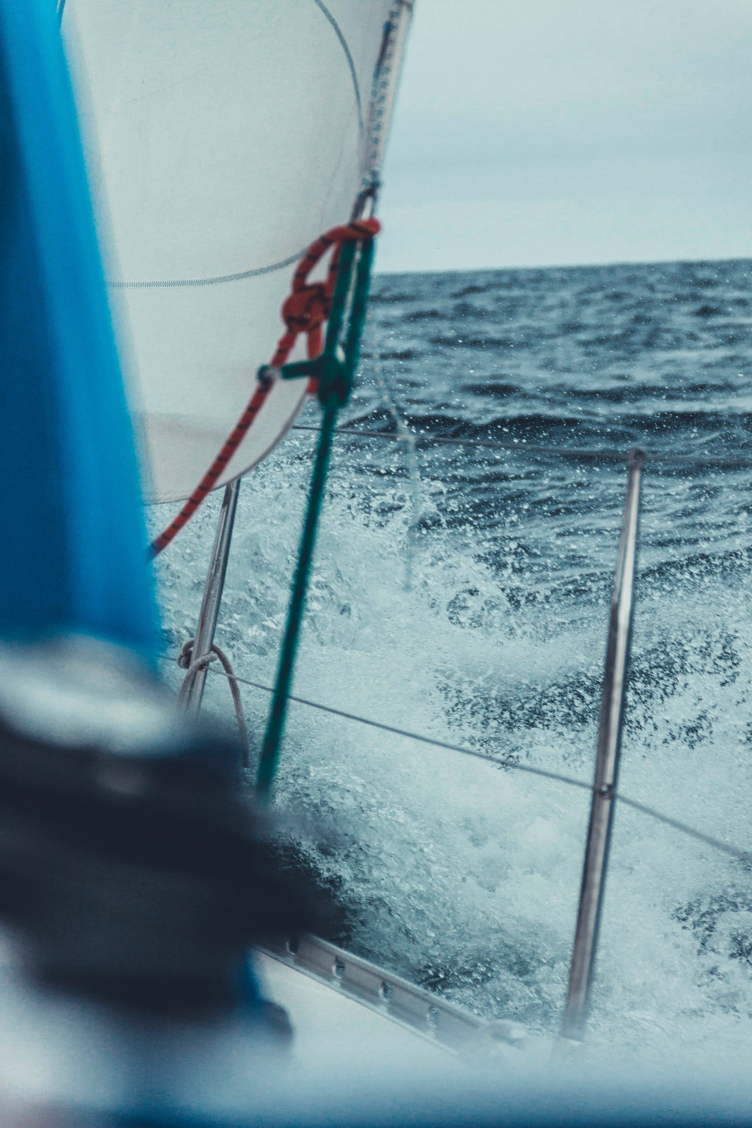 View from a boat showing the side of a sailboat with water splashing behind as it moves through the ocean.