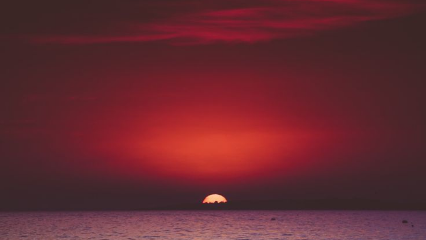 Un coucher de soleil avec un ciel rose et rouge au-dessus de l'océan.