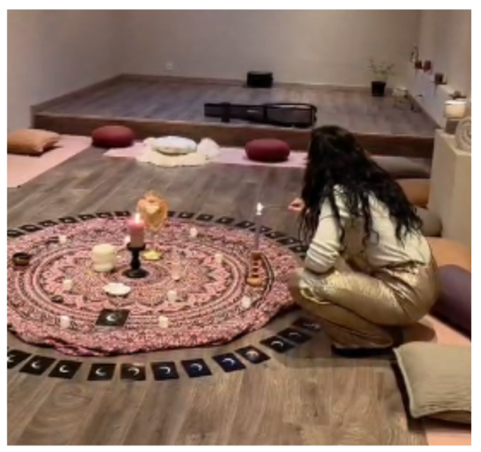 Une femme pratique une séance de tarot ou de méditation dans une pièce calme avec un tapis rond, bougies, cristaux et cartes de tarot.