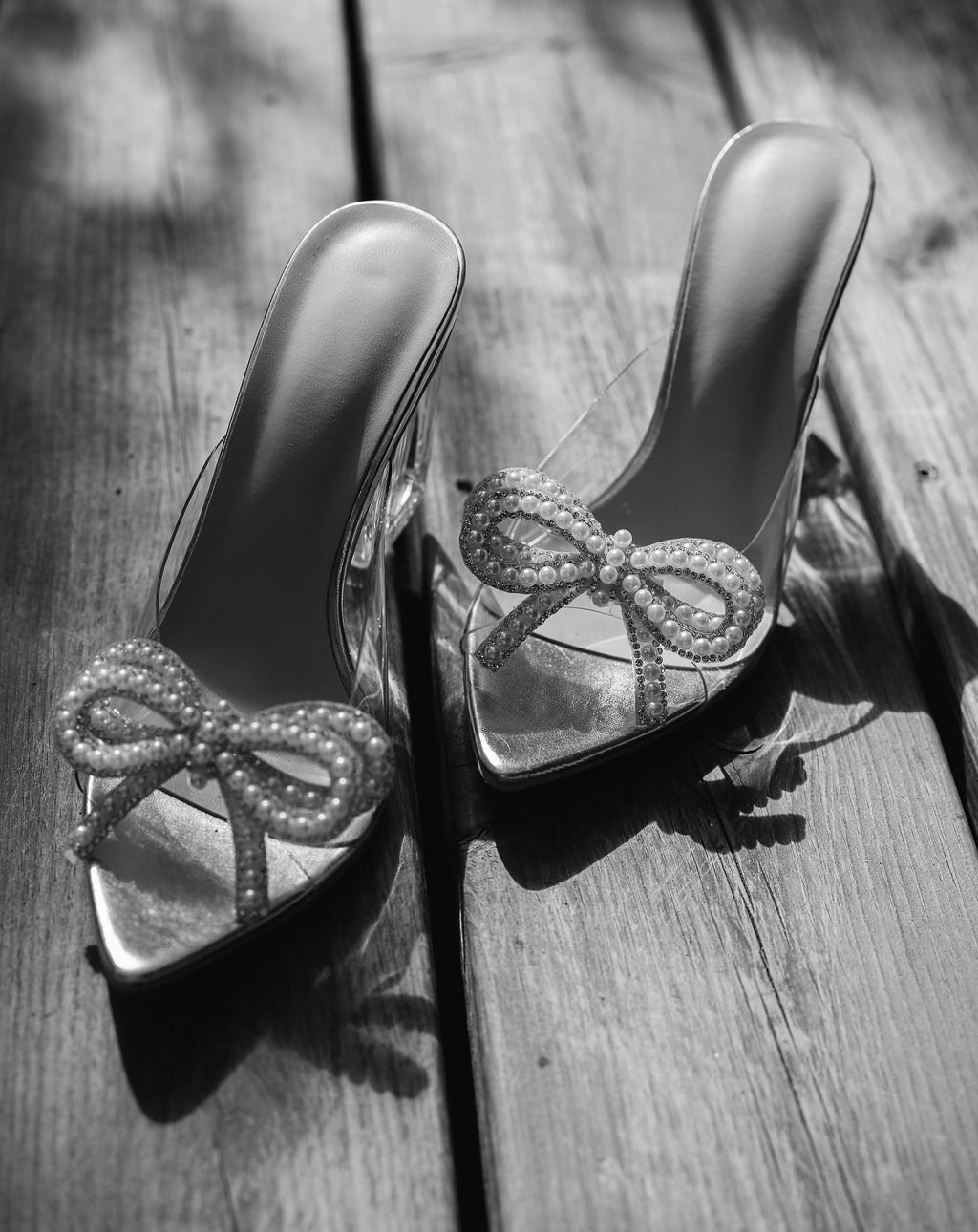 Chaussures à talons hauts décorées d'un nœud en perles, posées sur un plancher en bois.