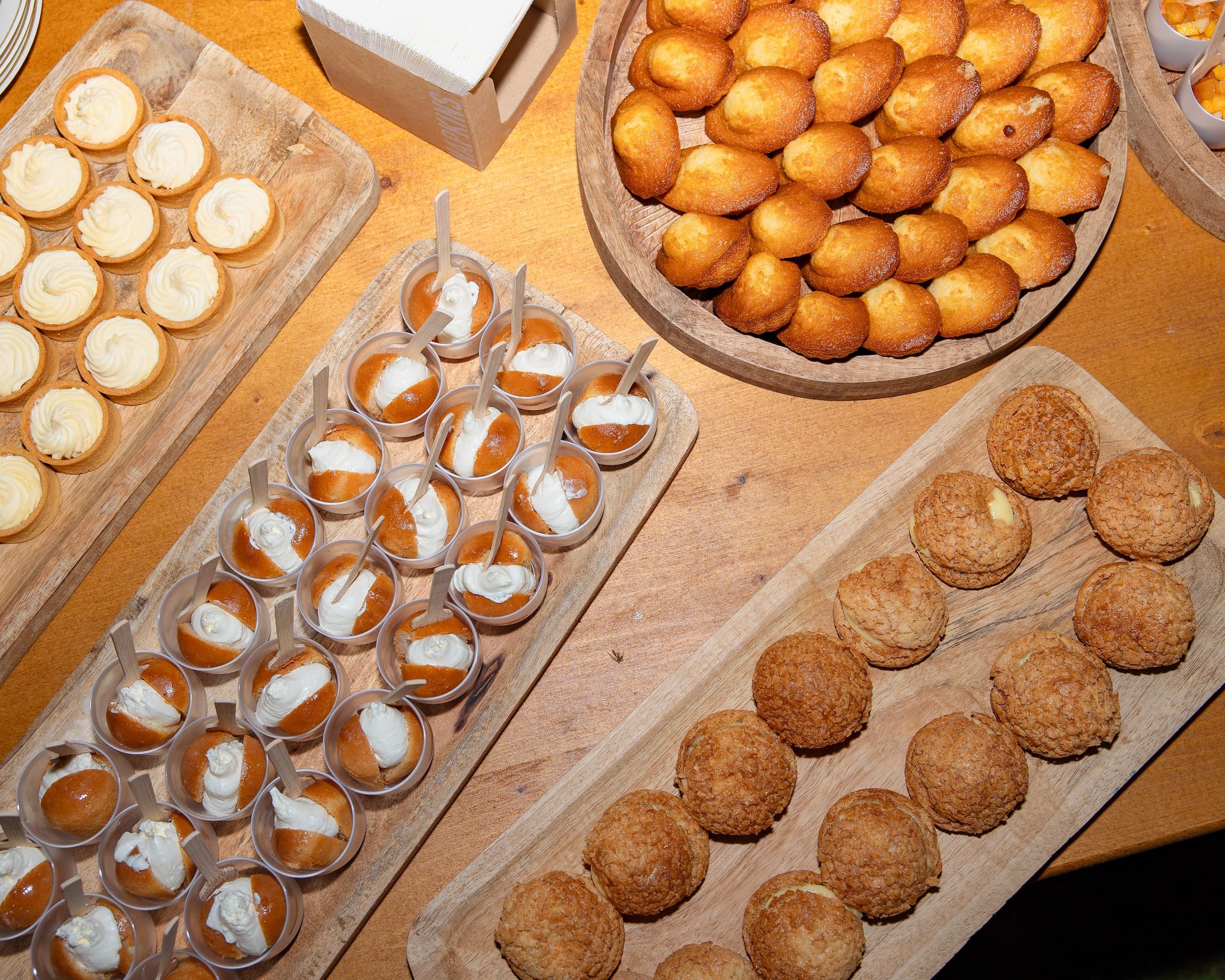 Assortiment de desserts : tartelettes au citron, bouchées à la crème, beignets, et biscuits croustillants sur des plateaux en bois.