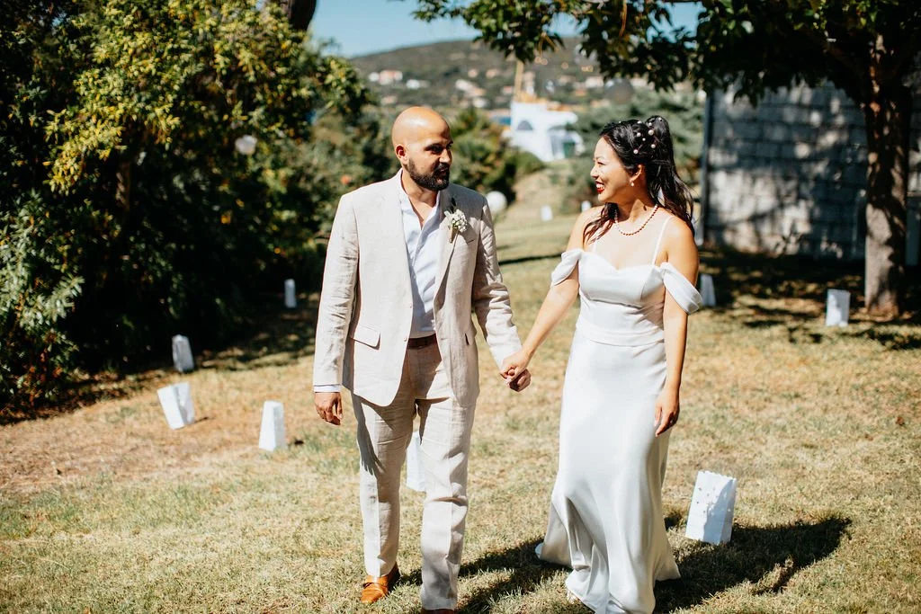 Un couple en habits de mariage qui se tient la main dans un jardin ensoleillé.