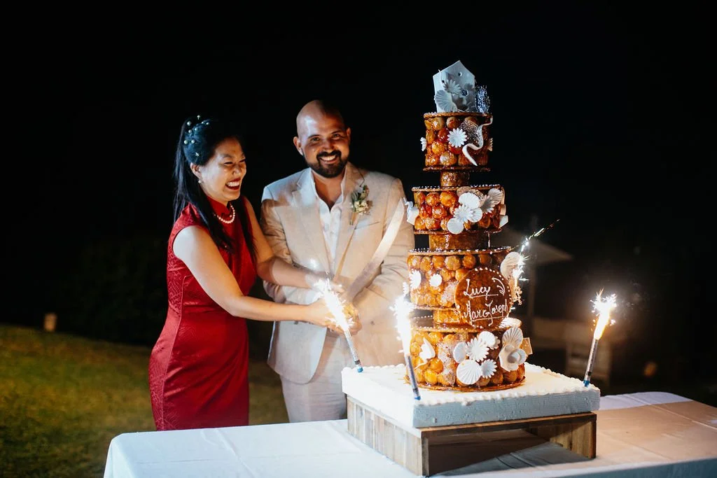 Un couple souriant coupe un gâteau de mariage à l'extérieur la nuit, avec des feux d'artifice