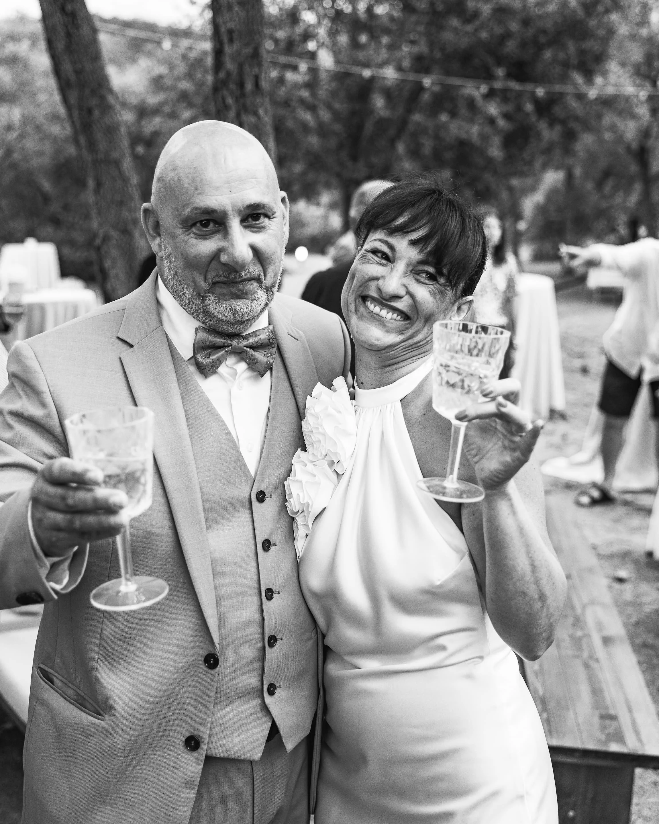 Deux personnes souriantes portant des verres de boisson, lors d'une célébration en plein air.
