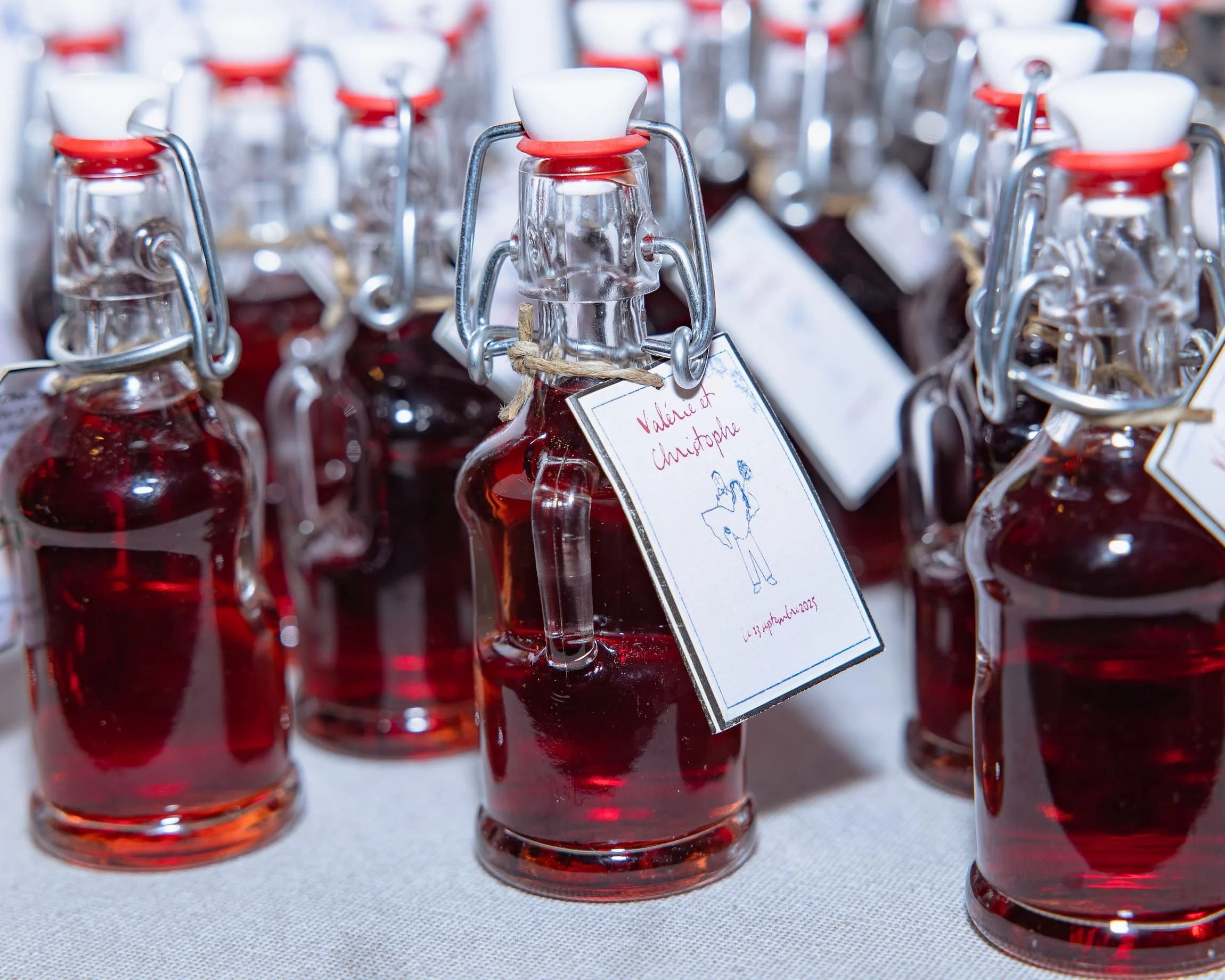 Bouteilles en verre contenant une boisson rouge, avec étiquettes manuscrites, sur une table. 