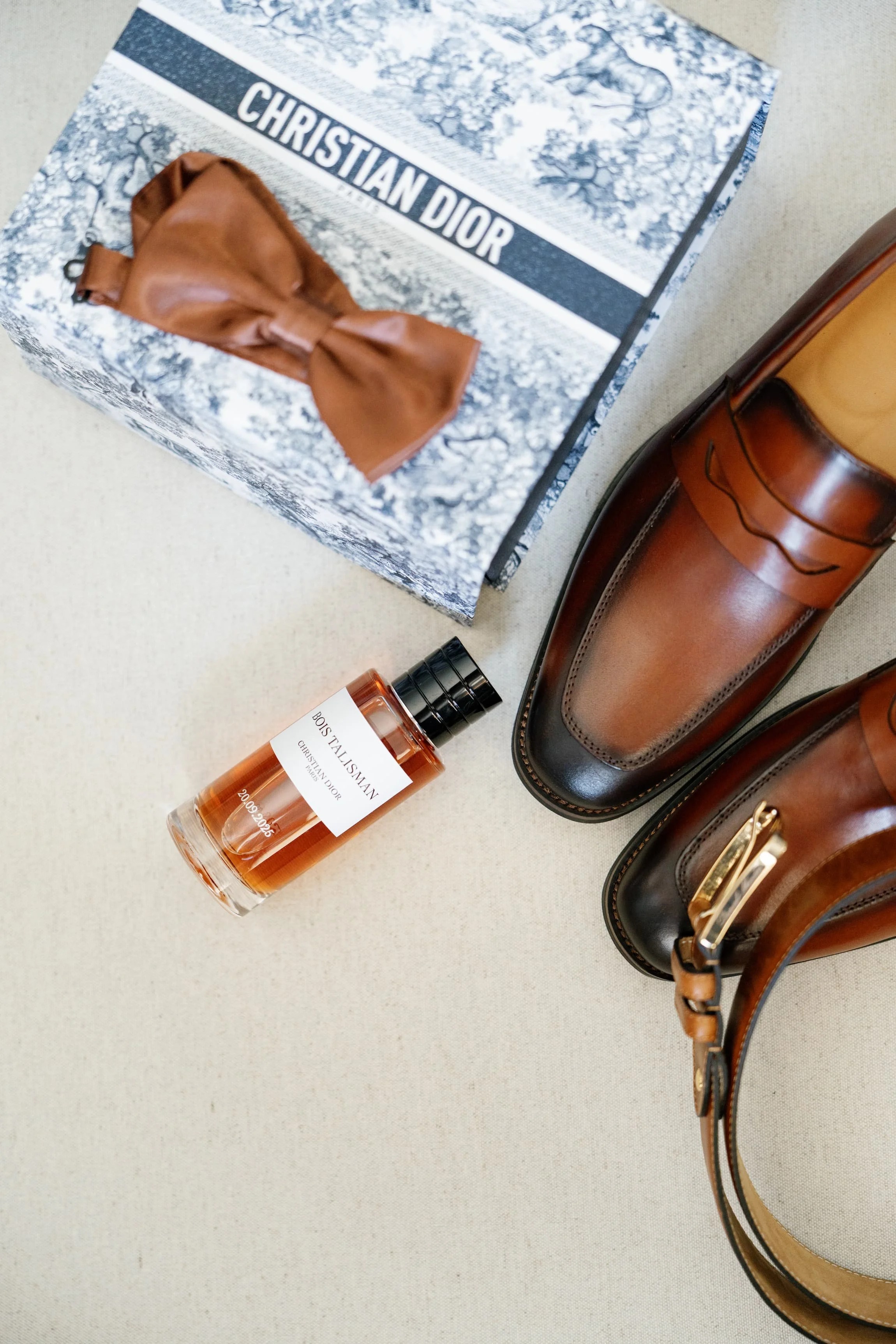 Une boîte de Christian Dior, une paire de bottes en cuir marron et noir, un flacon de parfum Dior, et un sac à main en cuir marron