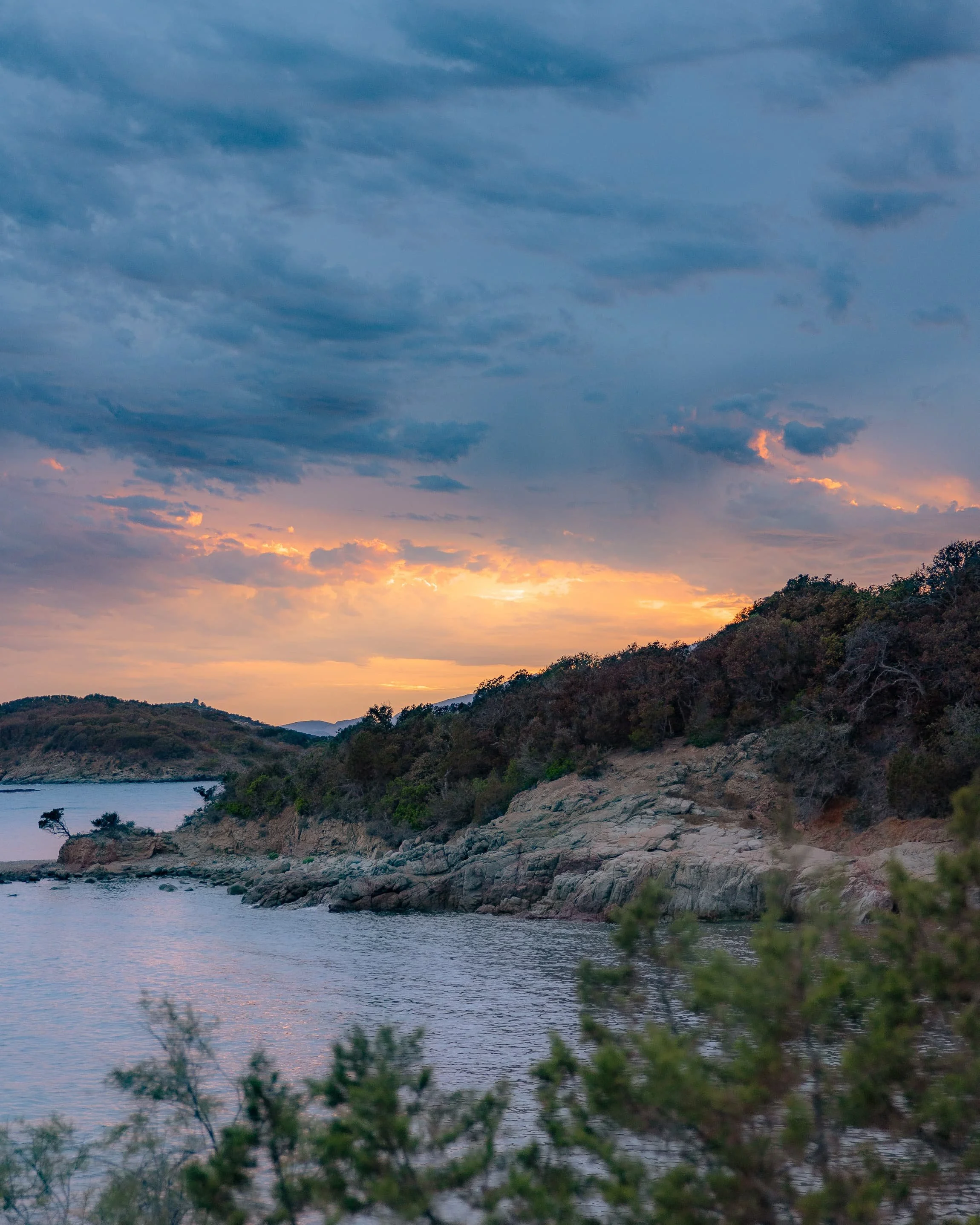 Coucher de soleil sur une rivière bordée de collines avec des arbres et des nuages dans le ciel.
