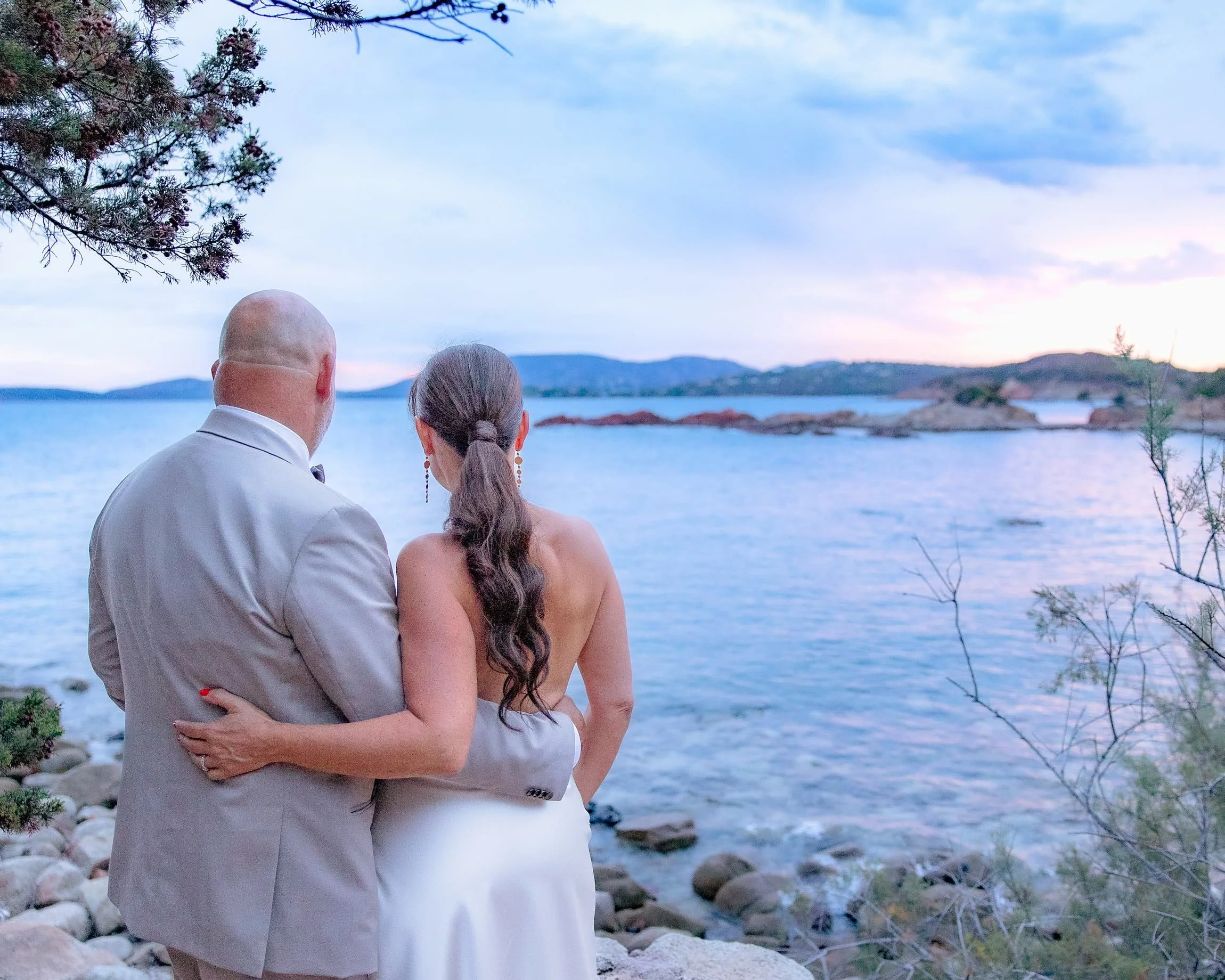 Un couple habillé élégamment, près d'un lac, regardant vers l'horizon au coucher du soleil.