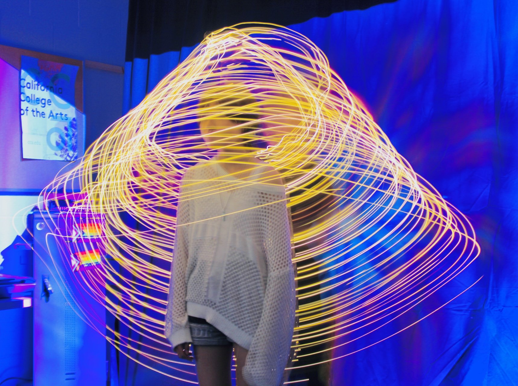 Person standing in front of a light painting display with swirling yellow light trails at California College of the Arts.