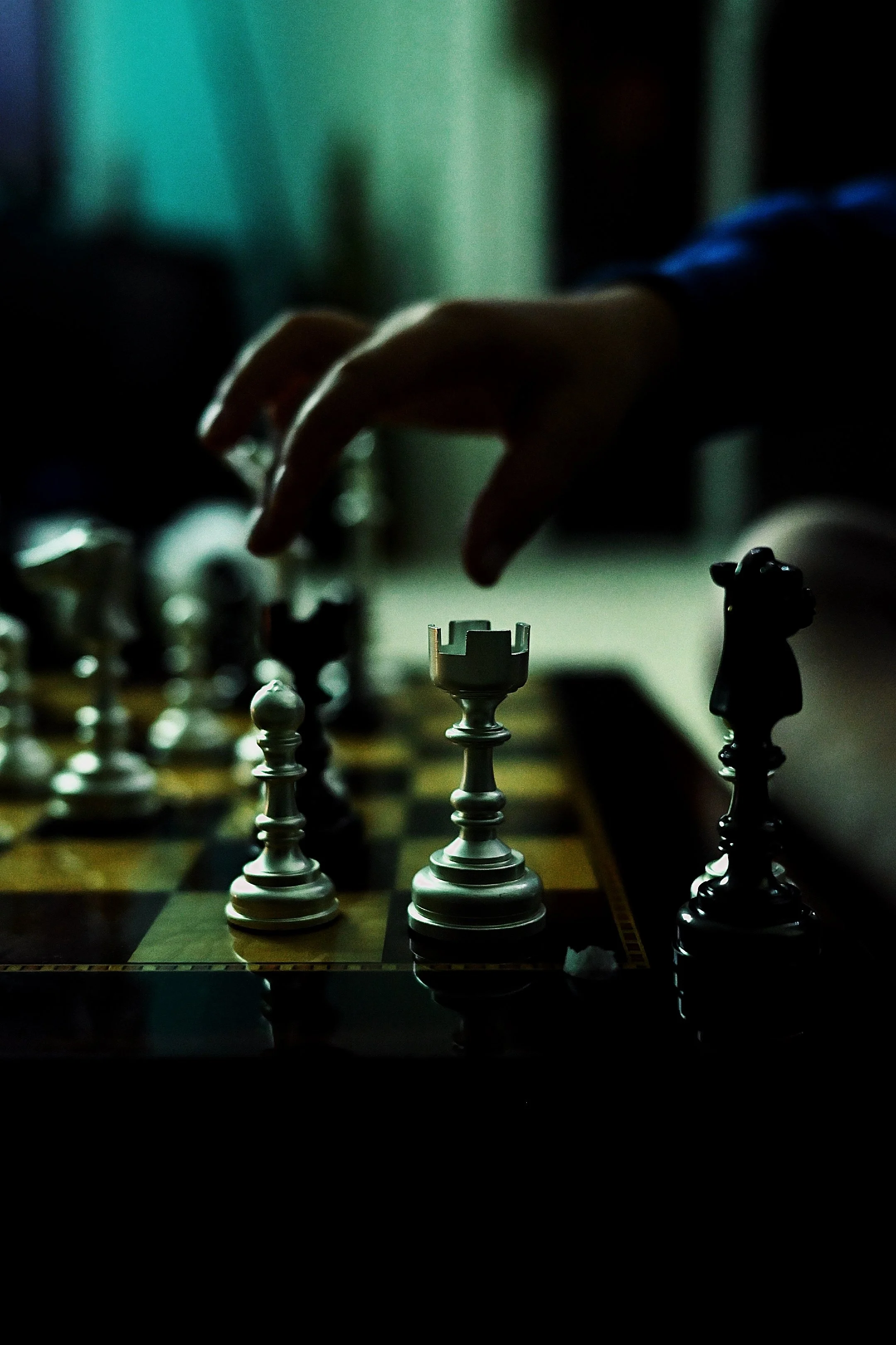 A person playing chess, moving a white rook on the board in a dimly lit room.