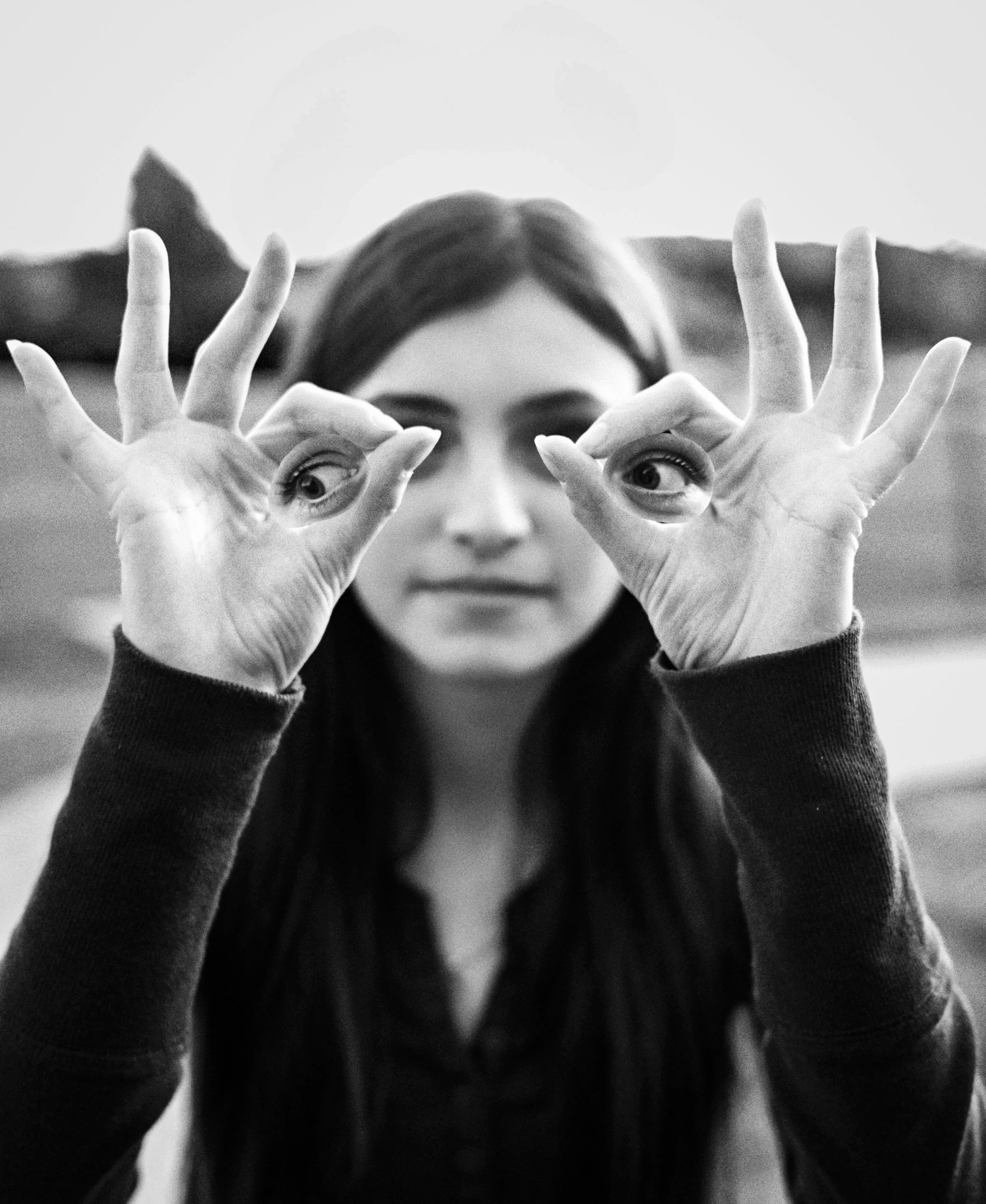 Black and white photo of a young woman holding her hands up to her face with her fingers in circular shapes around her eyes, looking through the shapes.