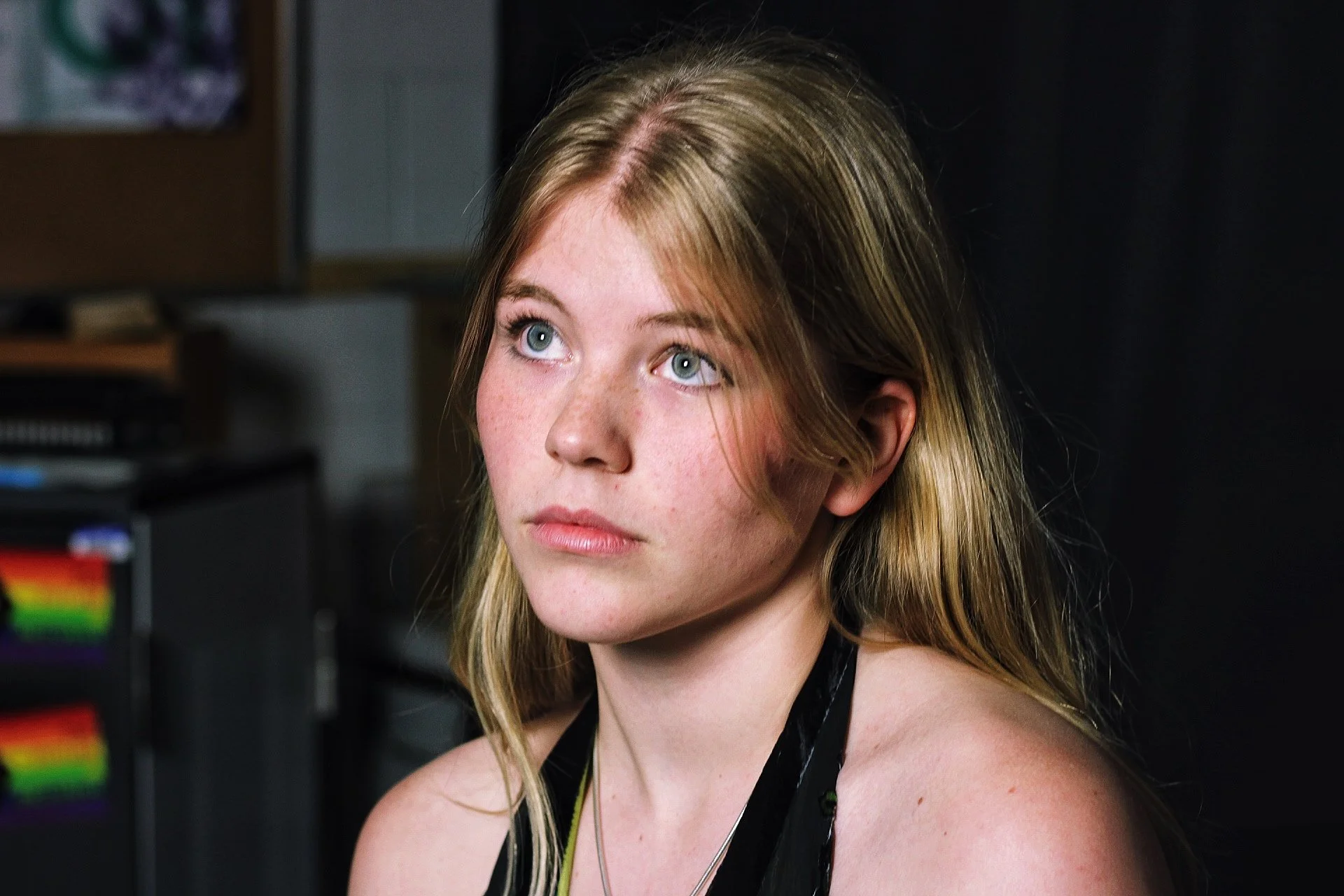 A young woman with long blonde hair and fair skin, looking to her left with a neutral expression.