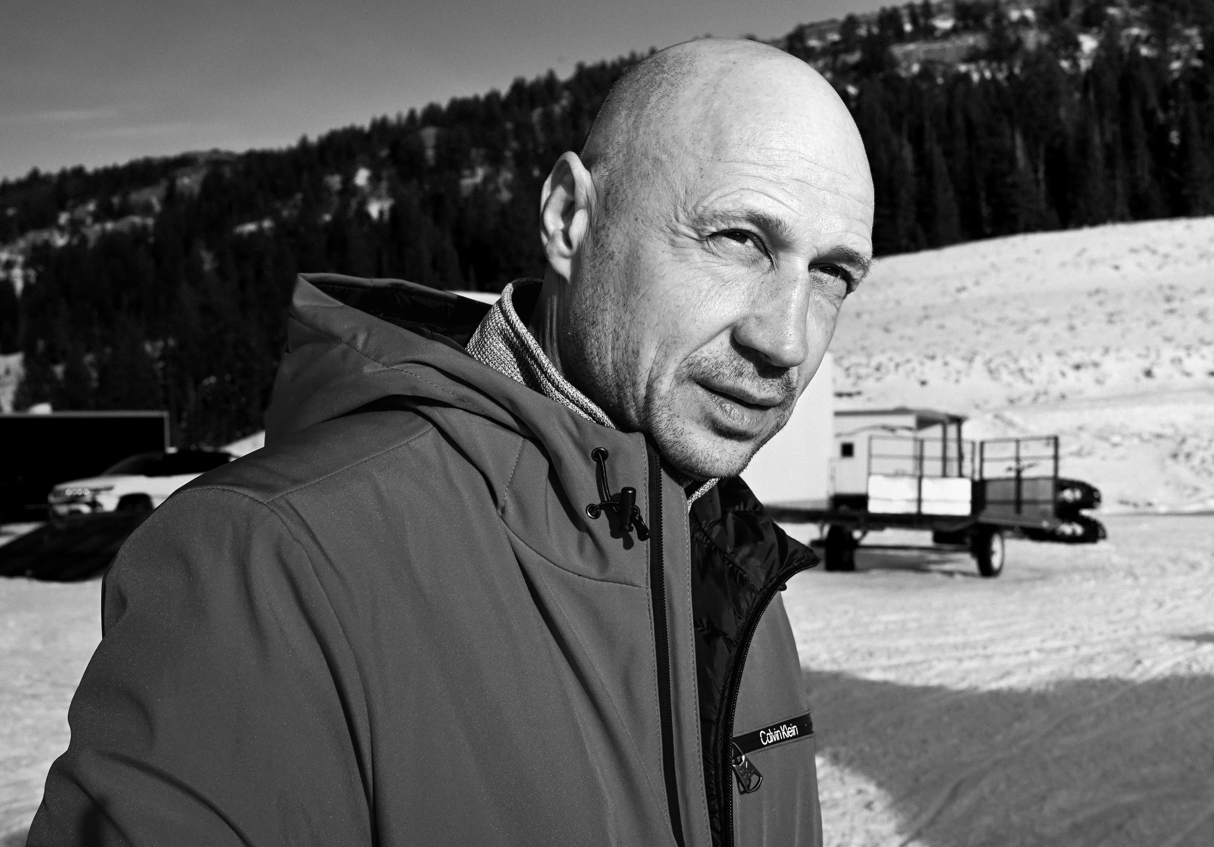 A middle-aged man with a fierce expression in a snowy outdoor setting, wearing a Calvin Klein jacket.