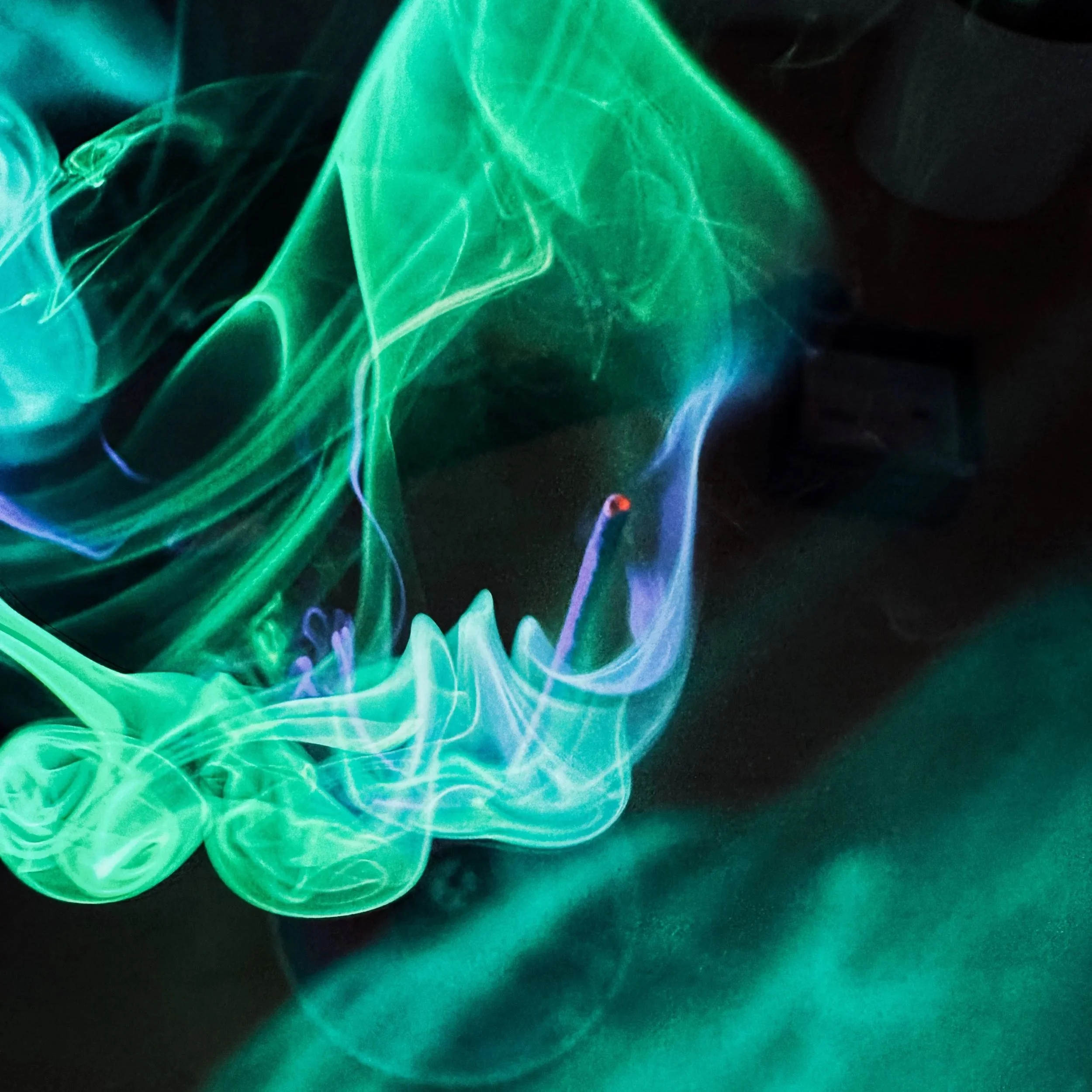 Colorful swirling smoke in shades of green, blue, and purple against a dark background.