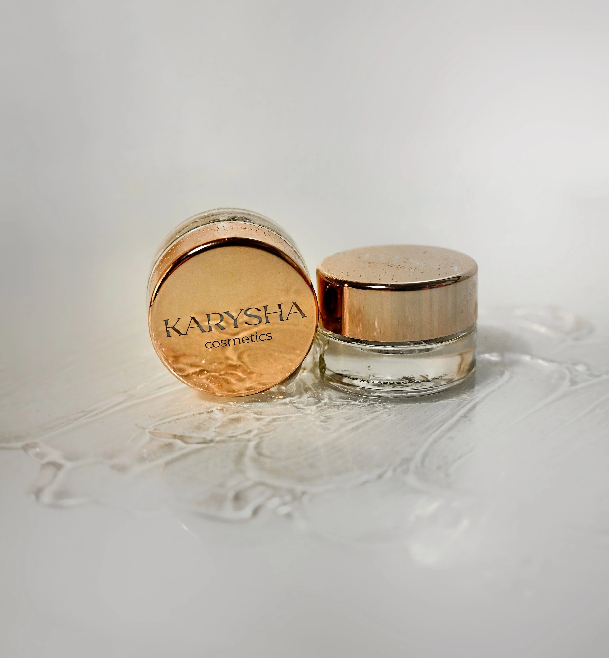 Two Karysha cosmetics jars with rose gold lids placed on a white textured surface.
