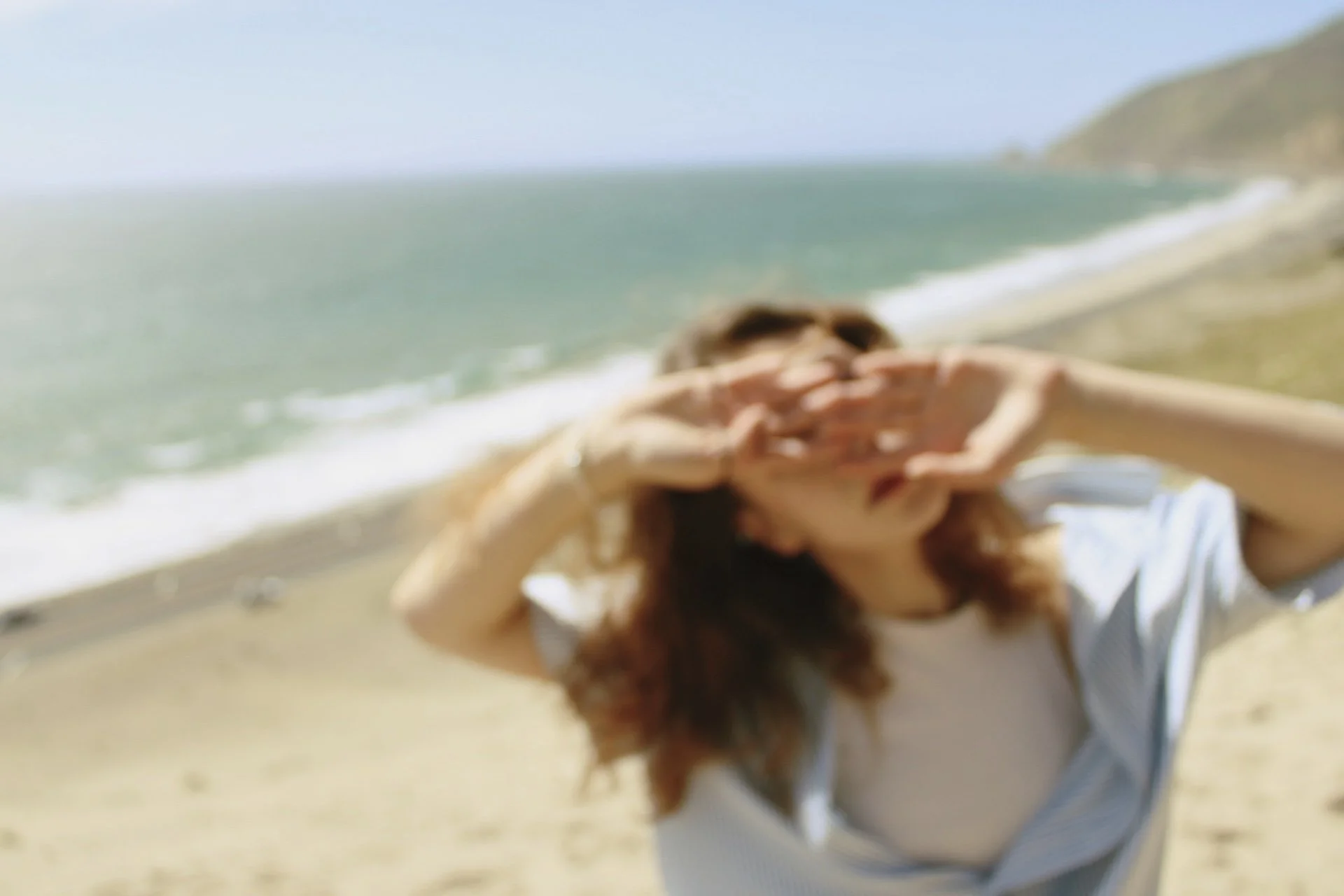 Blurred image of a woman on a beach, shielding her eyes from the sun with her hands.