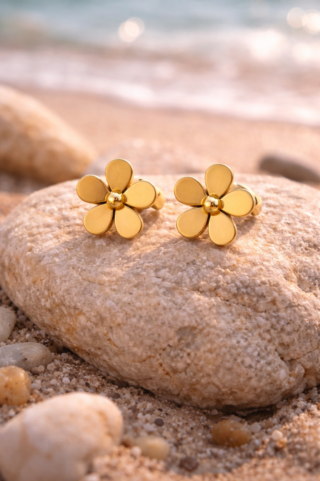 Gold flower earrings on sunlit rock.png