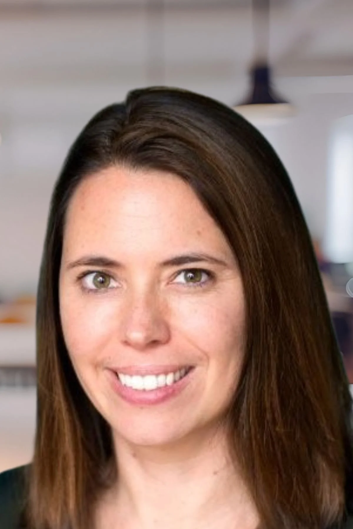 A smiling woman with long brown hair and green eyes, in an indoor setting.