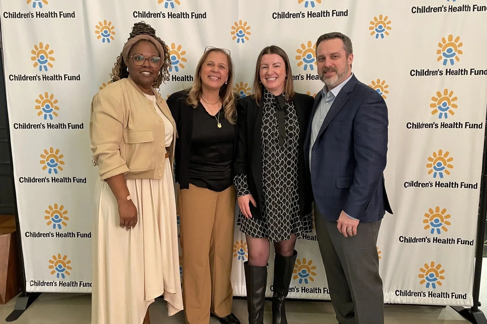 Four people standing together in front of a backdrop with the Children's Health Fund logo, smiling for the camera.
