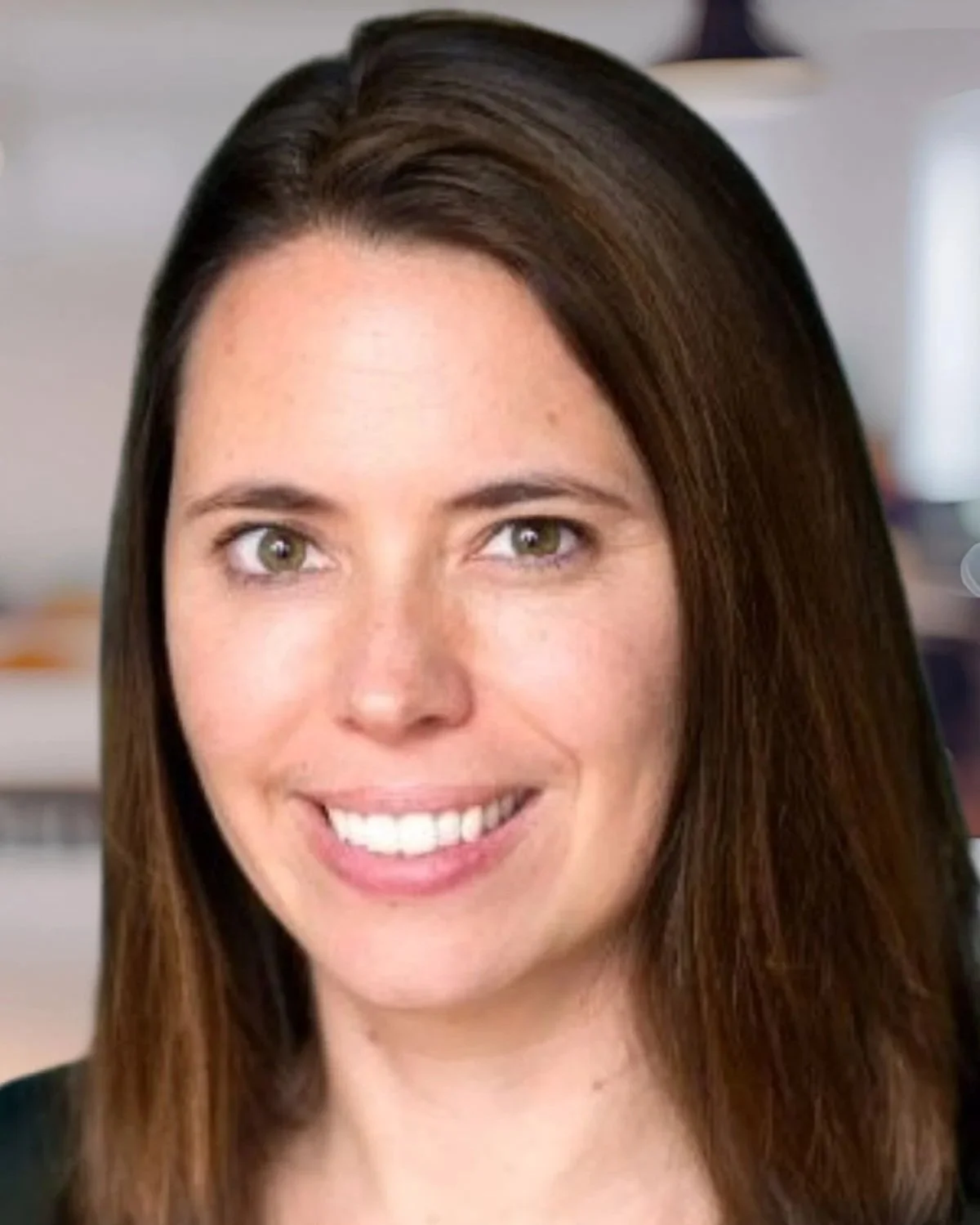 A woman with long brown hair smiling, showing her teeth, in an indoor setting.
