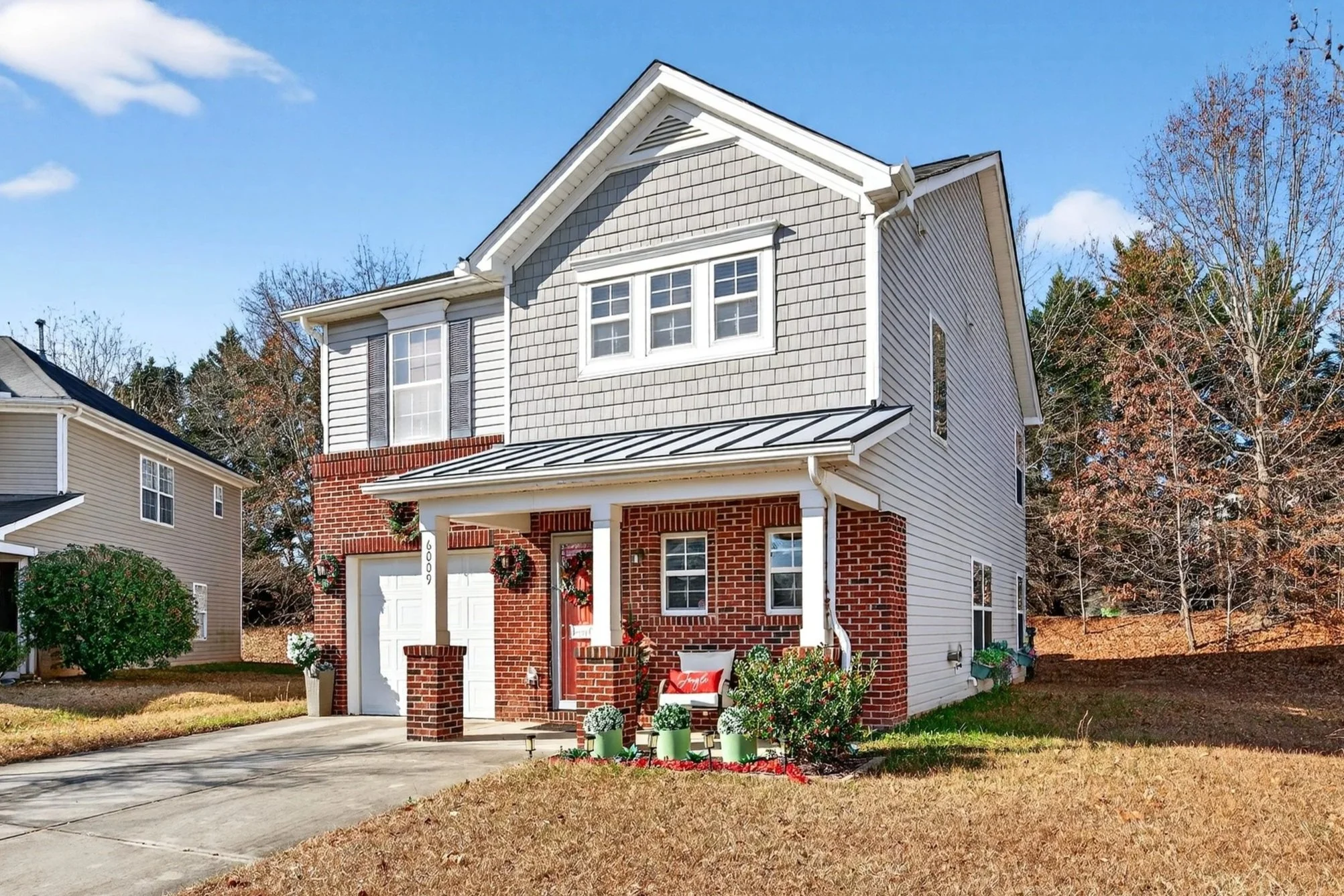 A two-story house with a brick and beige siding exterior, decorated for Christmas, with a concrete driveway, front porch, and fall foliage in the yard. Real estate photography pro, Raleigh NC