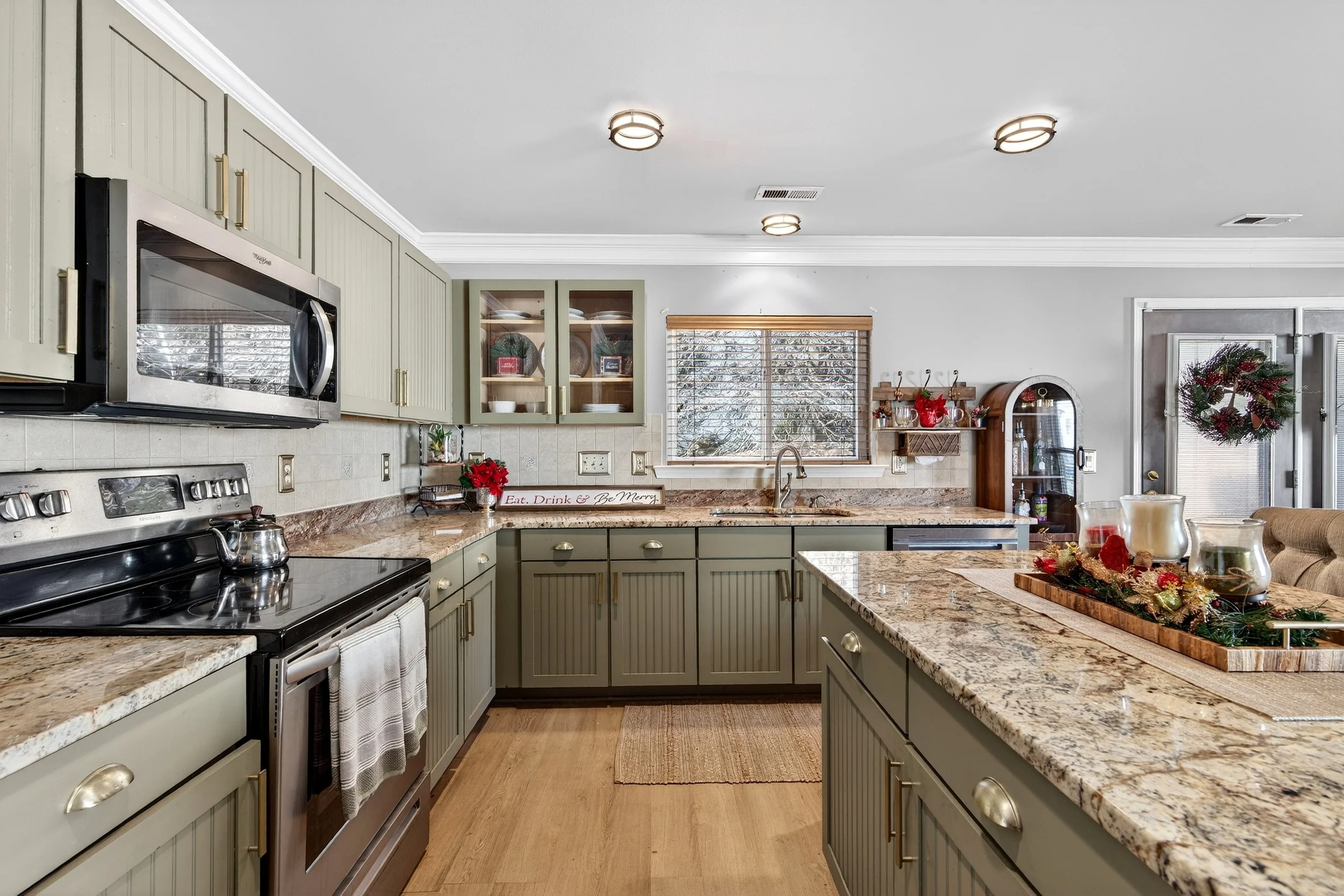 Kitchen with sage green cabinets, granite countertops, a stainless steel stove and microwave, decorated with Christmas ornaments and wreath, illuminated by ceiling lights. Real estate photography pro, Raleigh NC