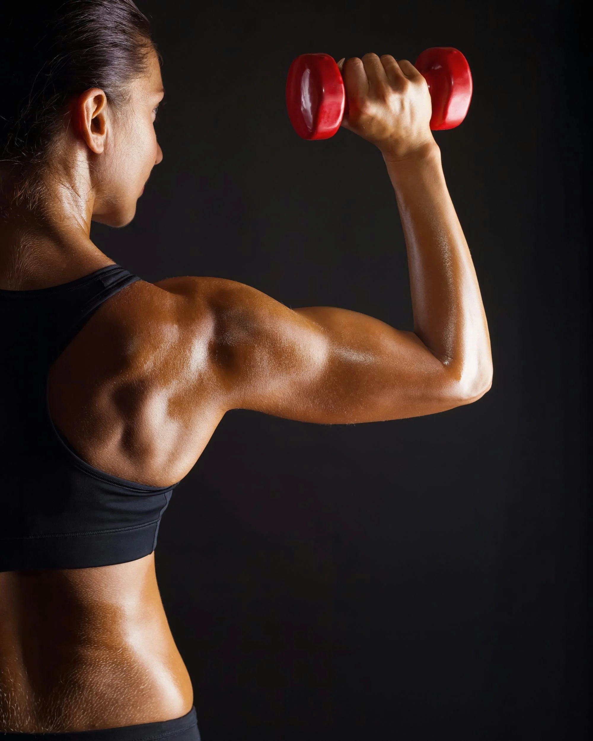 A woman lifting a red dumbbell, showing her muscular arm and shoulder against a dark background.