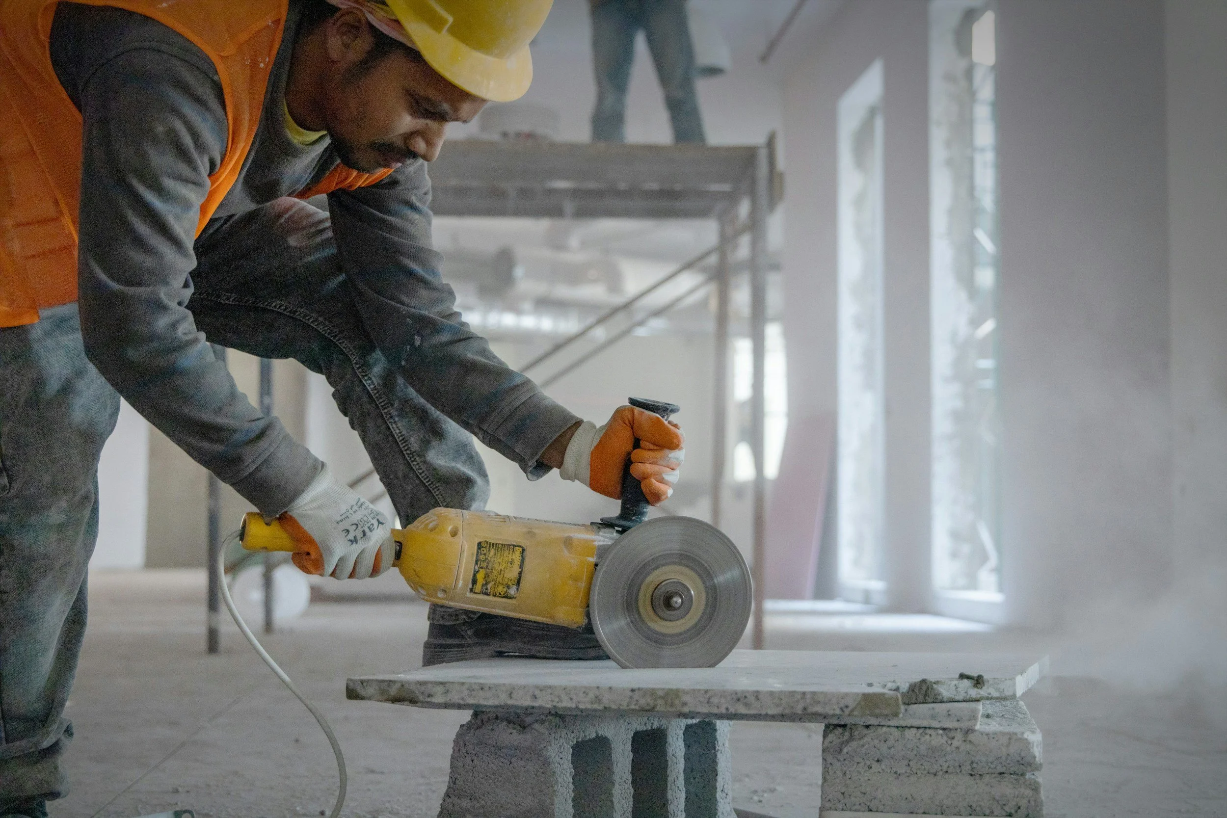 A construction worker cutting a stone slab with a handheld power circular saw inside a building under construction.