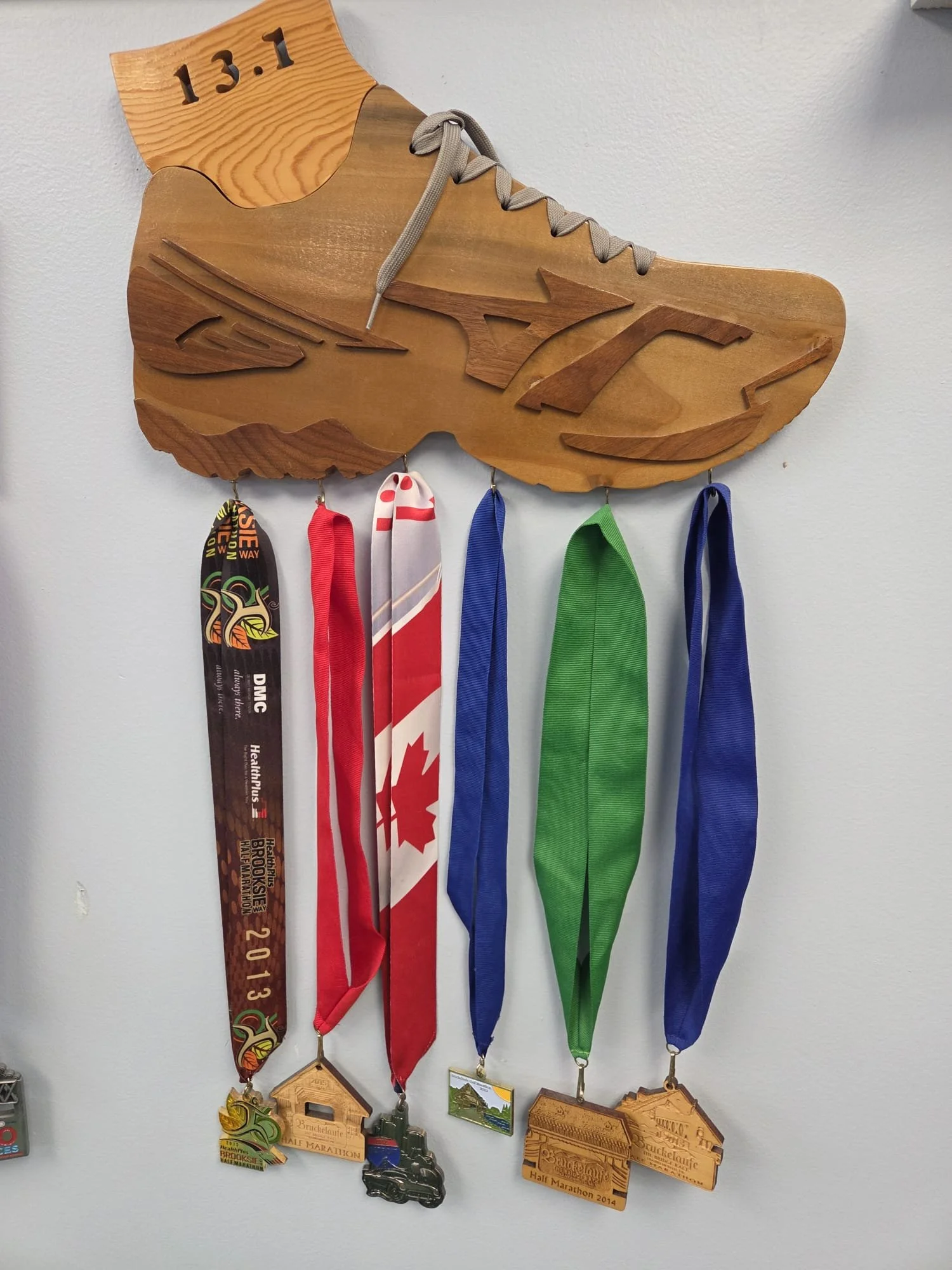 Wooden shoe-shaped display with five half marathon medals hanging from it, each with distinct ribbons and medals.