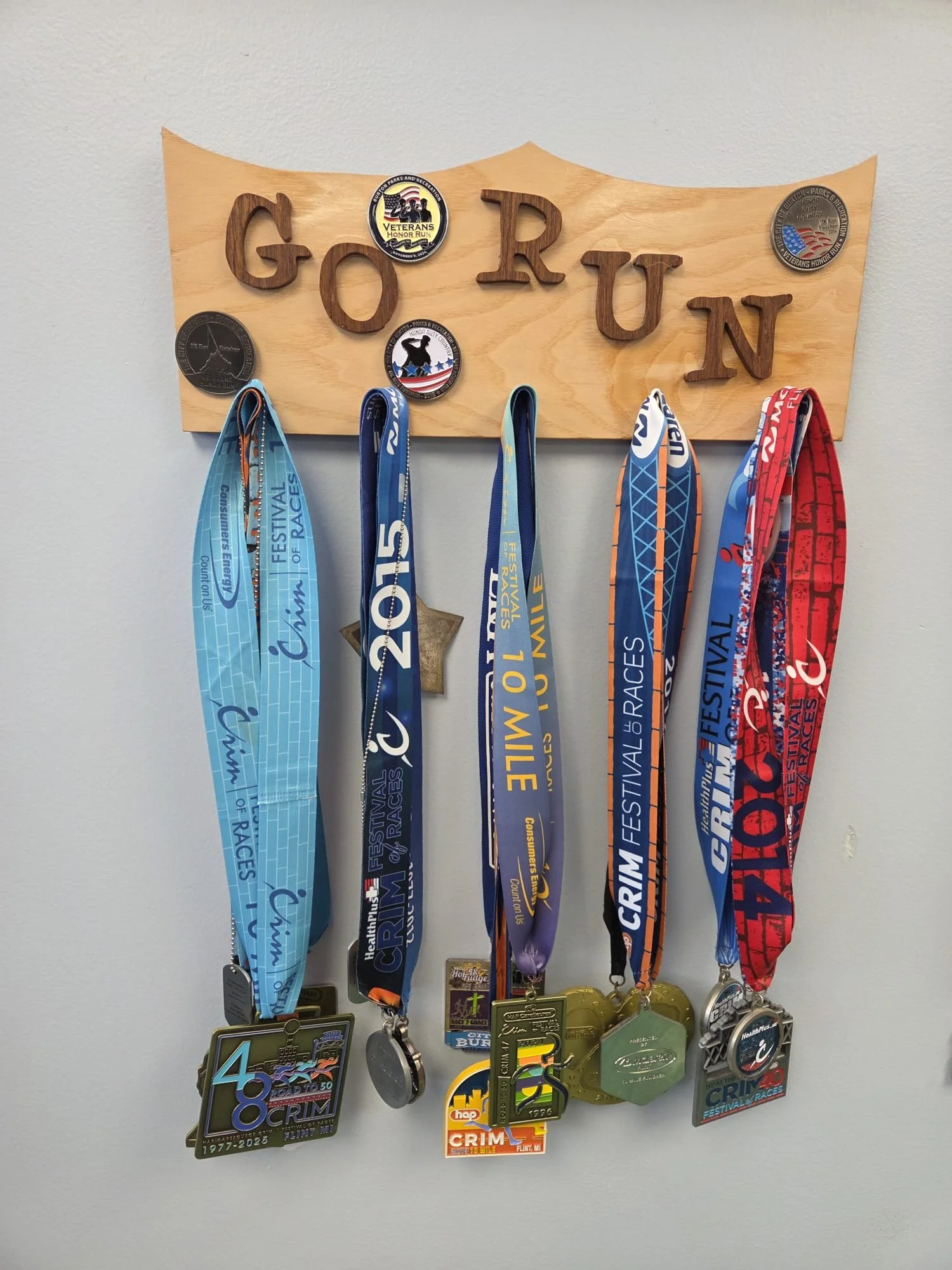 A wooden sign with the word "GO RUN" and badges and medals hanging below it from various races and events, including the Crim Festival of Races.