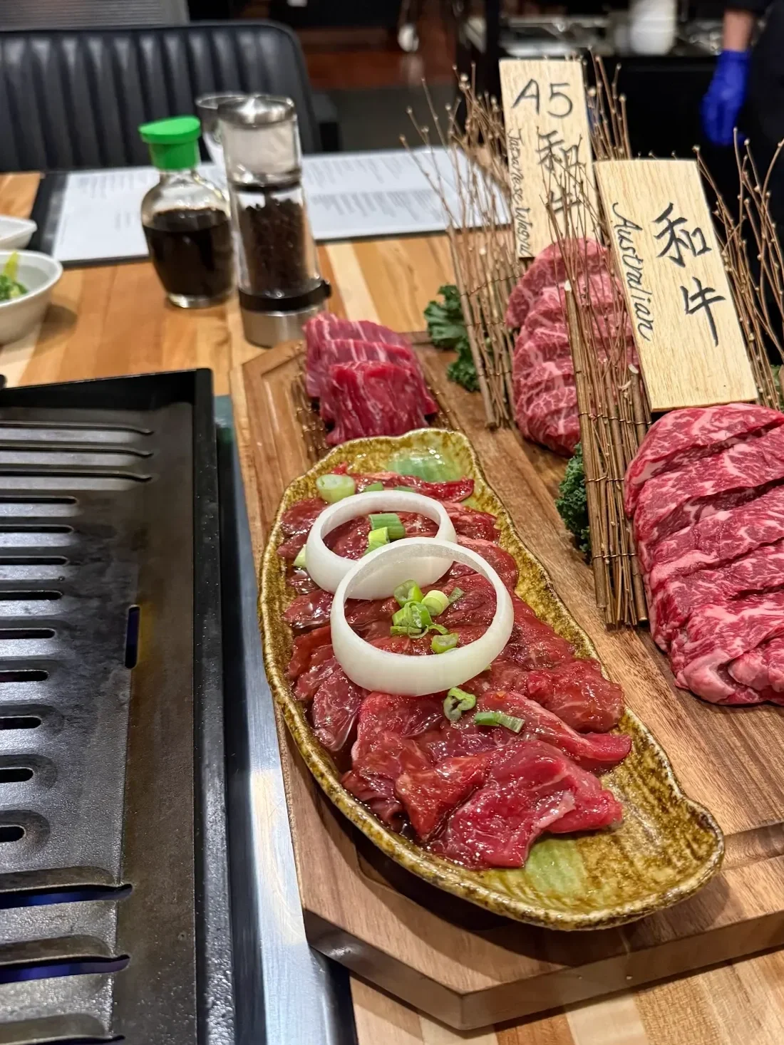 Variety of raw beef cuts on a wooden platter with sliced onions and green onions, at a Japanese yakiniku restaurant.