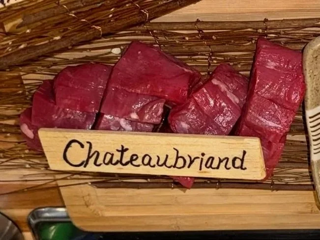 Slices of raw red meat on a platter with a wooden label that reads "Chateaubriand."