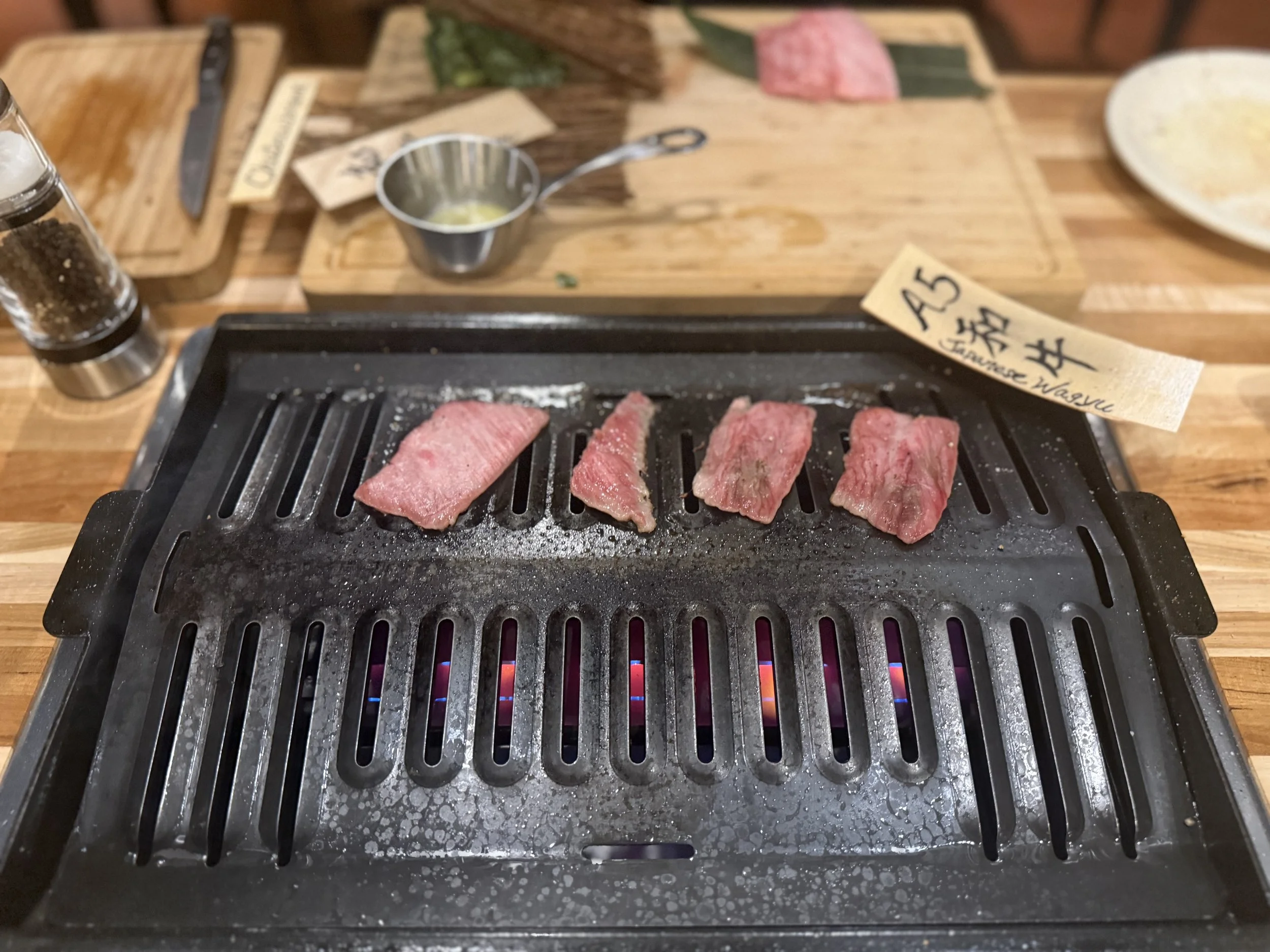 Five slices of raw beef steak cooking on a grill at a Japanese-style barbecue restaurant.