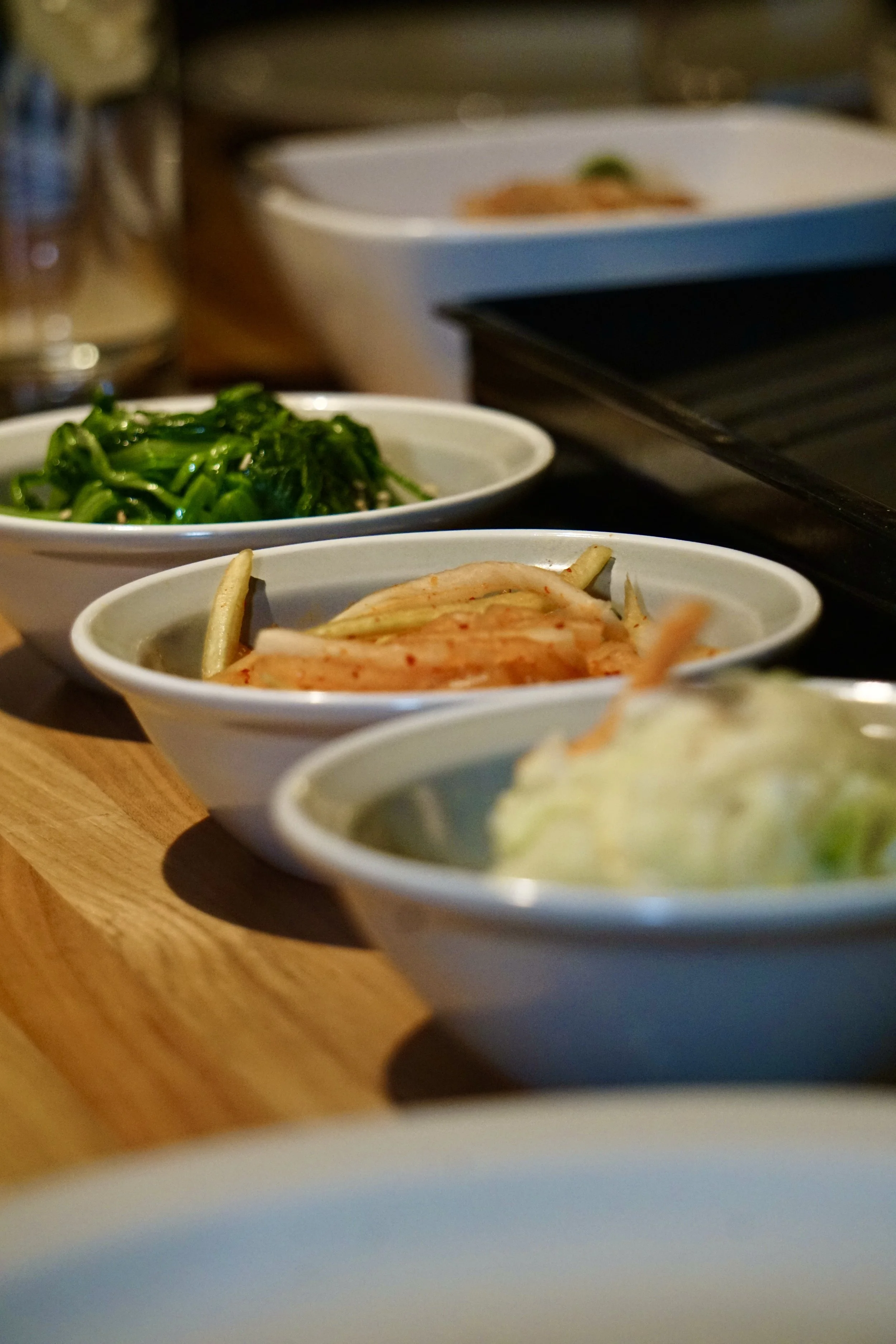 Three small bowls of food with vegetables on a wooden surface.