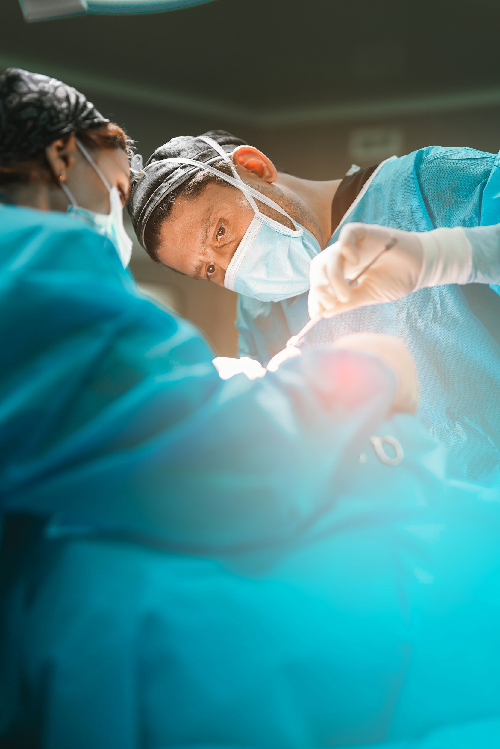 Two surgeons wearing masks, gloves, and scrubs perform a surgical procedure in an operating room.