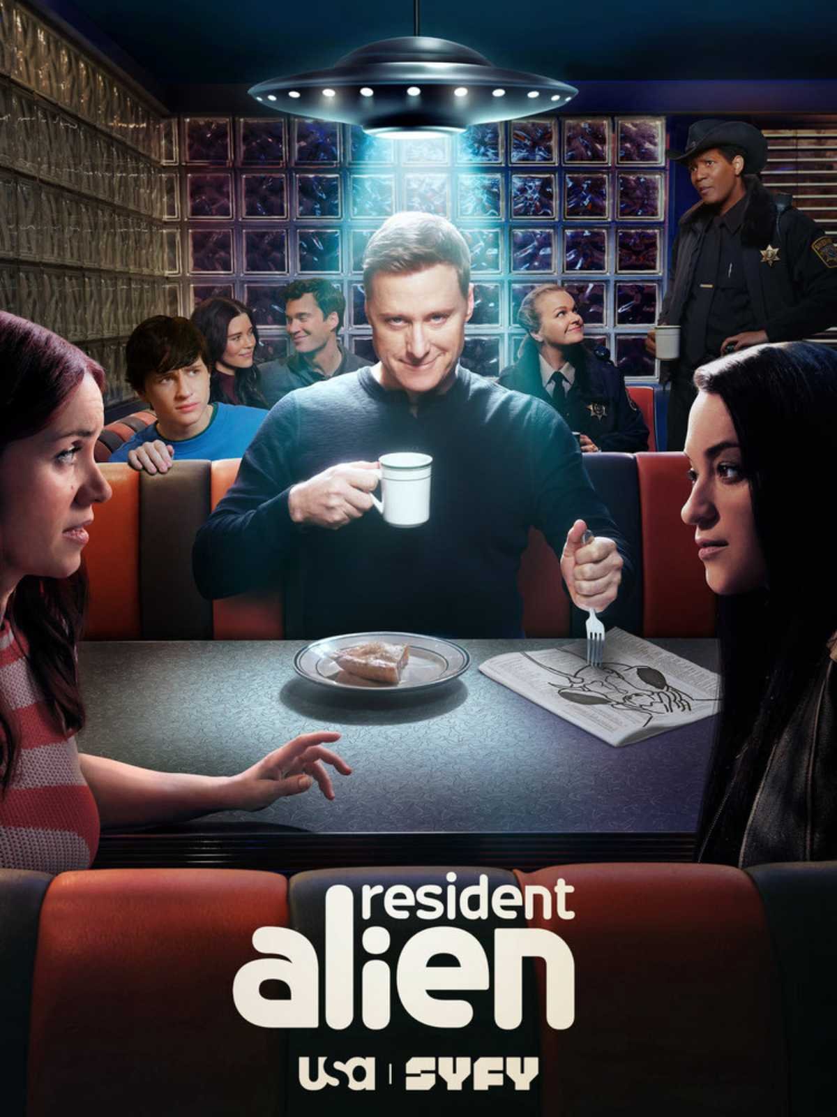 The promotional poster for the TV show 'Resident Alien' shows a man sitting at a diner table holding a coffee mug, with a slice of pie and a comic book in front of him. Several people, including police officers and civilians, are seated and standing behind him in a retro-style diner setting. The show's title and network are displayed at the bottom.