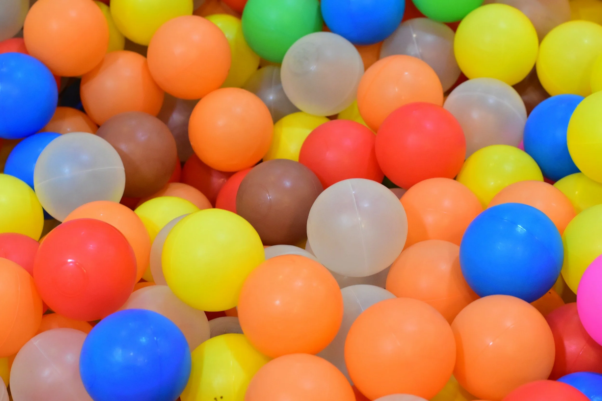 A colorful collection of plastic balls, including blue, yellow, orange, red, green, pink, brown, and white, with smooth surfaces.
